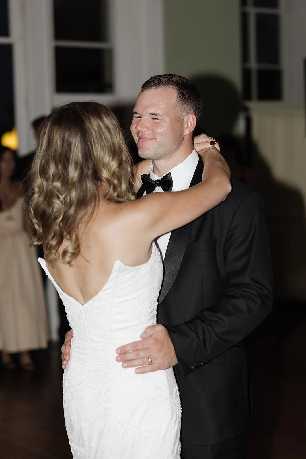 A bride and groom dancing closely at a wedding reception, with the bride wearing a white strapless gown and the groom in a black tuxedo.