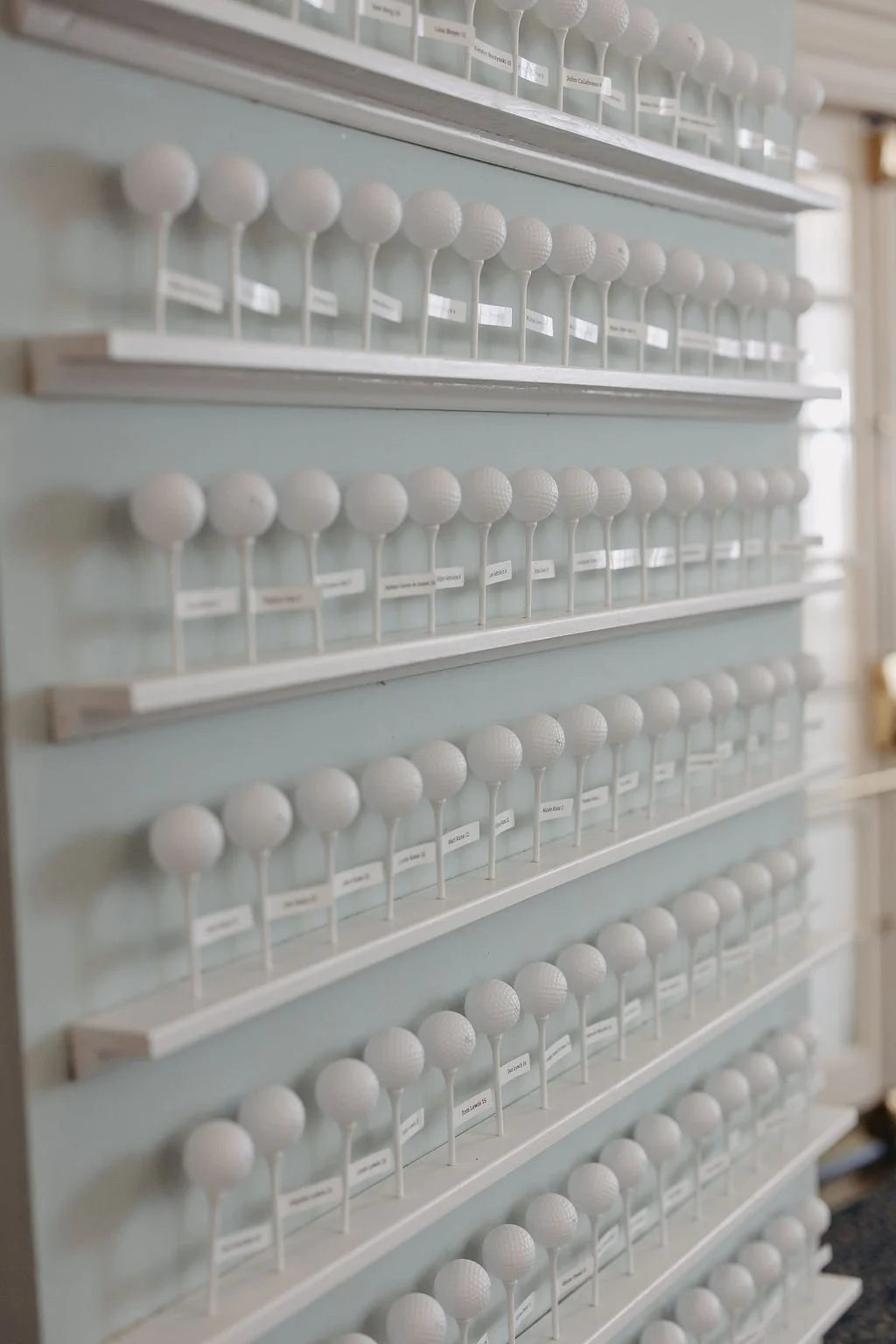 Display of multiple white golf balls arranged on shelves in a room.