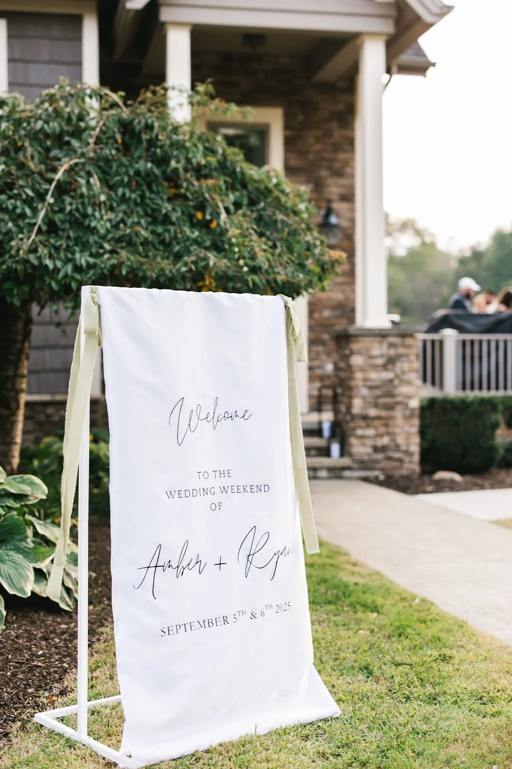 Wedding welcome sign outside a house, reading 'Welcome to the wedding weekend of Amber + Ryan, September 5th & 6th, 2025'.