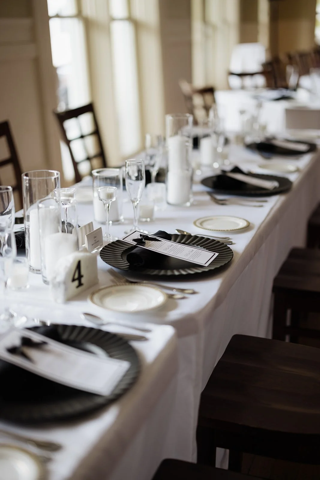 Elegant dining table set with black and white plates, silverware, multiple glasses, and candles, prepared for a formal event.