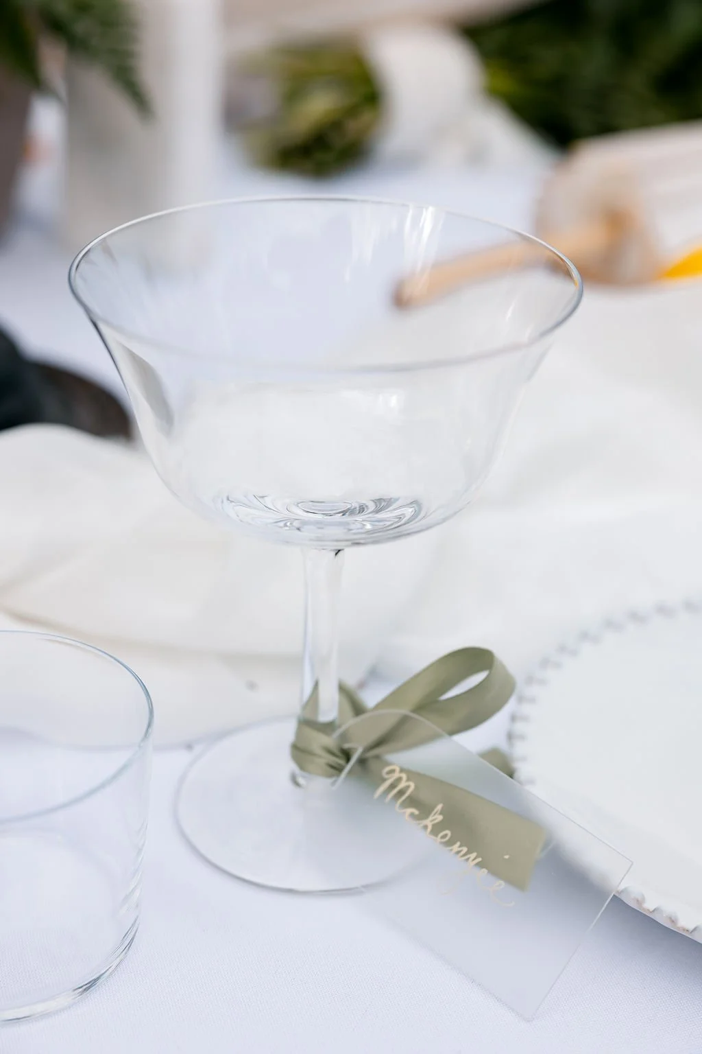 Empty clear cocktail glass with a ribbon and name tag on a white table.