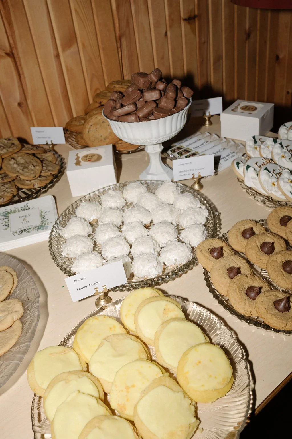 Assorted cookies and sweets on a dessert table at a celebration, including chocolate-covered candies, coconut snowballs, lemon drops, and decorated sugar cookies.