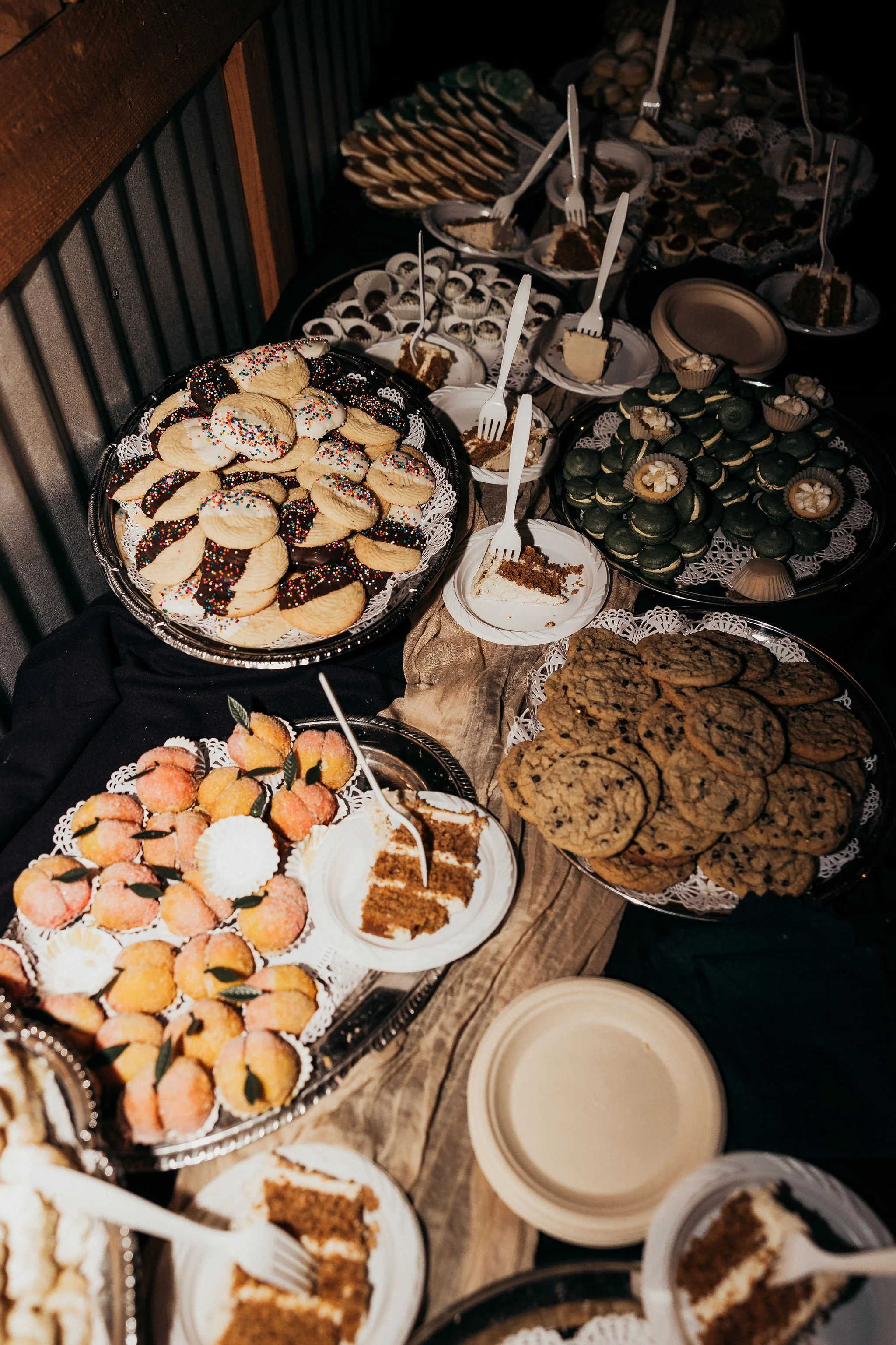 A variety of desserts on a table, including cookies, cupcakes, macarons, mini cakes, and slices of pie, some decorated with sprinkles and frosting.