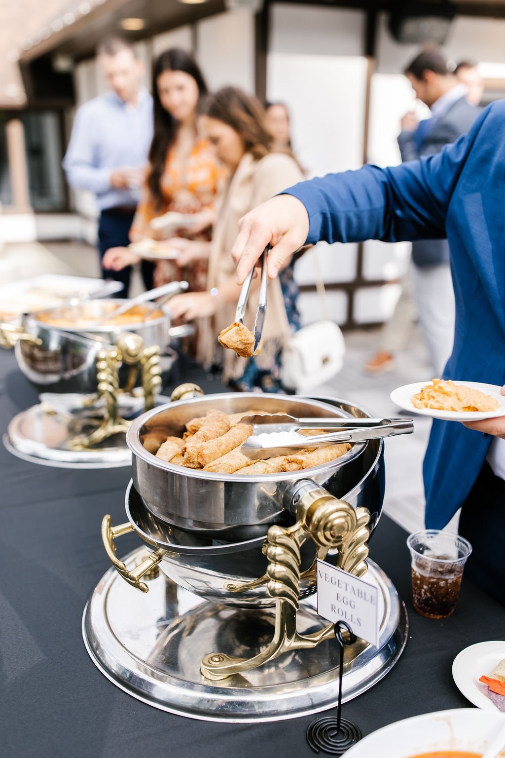 Buffet table with hot food, including vegetable egg rolls, at a social gathering.