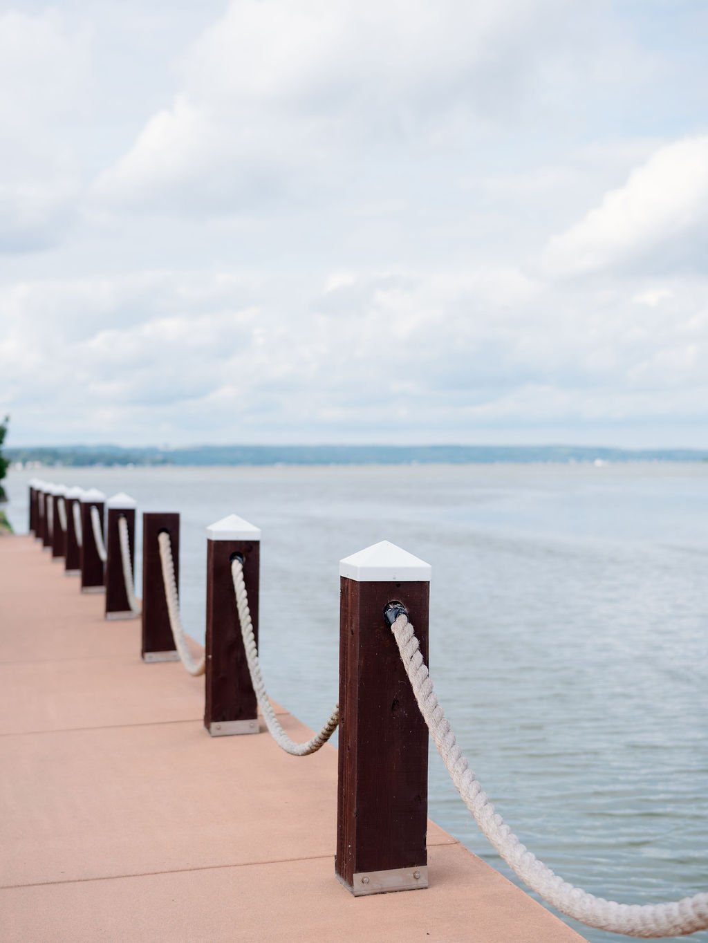 Wooden dock poles with white caps and rope railing along a lakeside or river on a cloudy day.