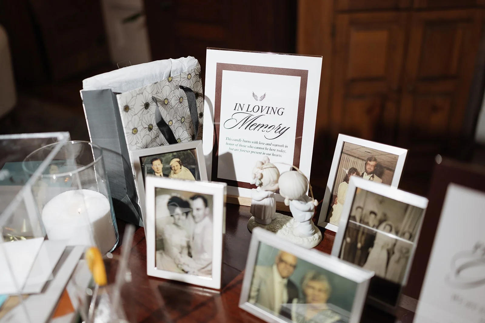 Memorial display with framed photographs of loved ones, candles, and a sign that says "In Loving Memories," on a wooden table.