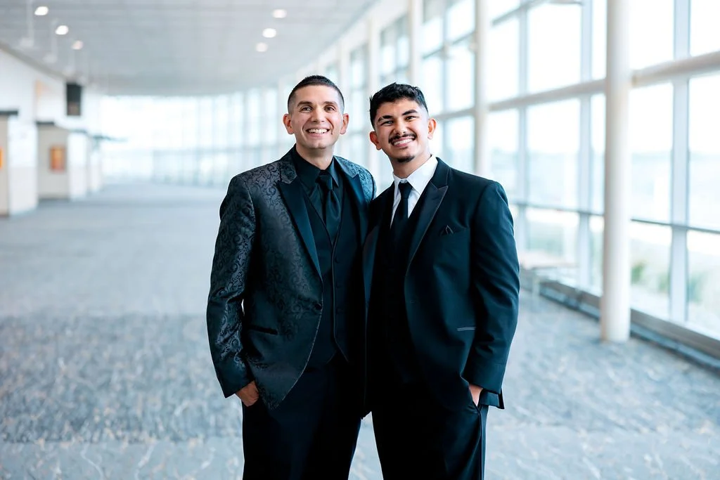 Two men in suits smiling inside a modern building with large windows.