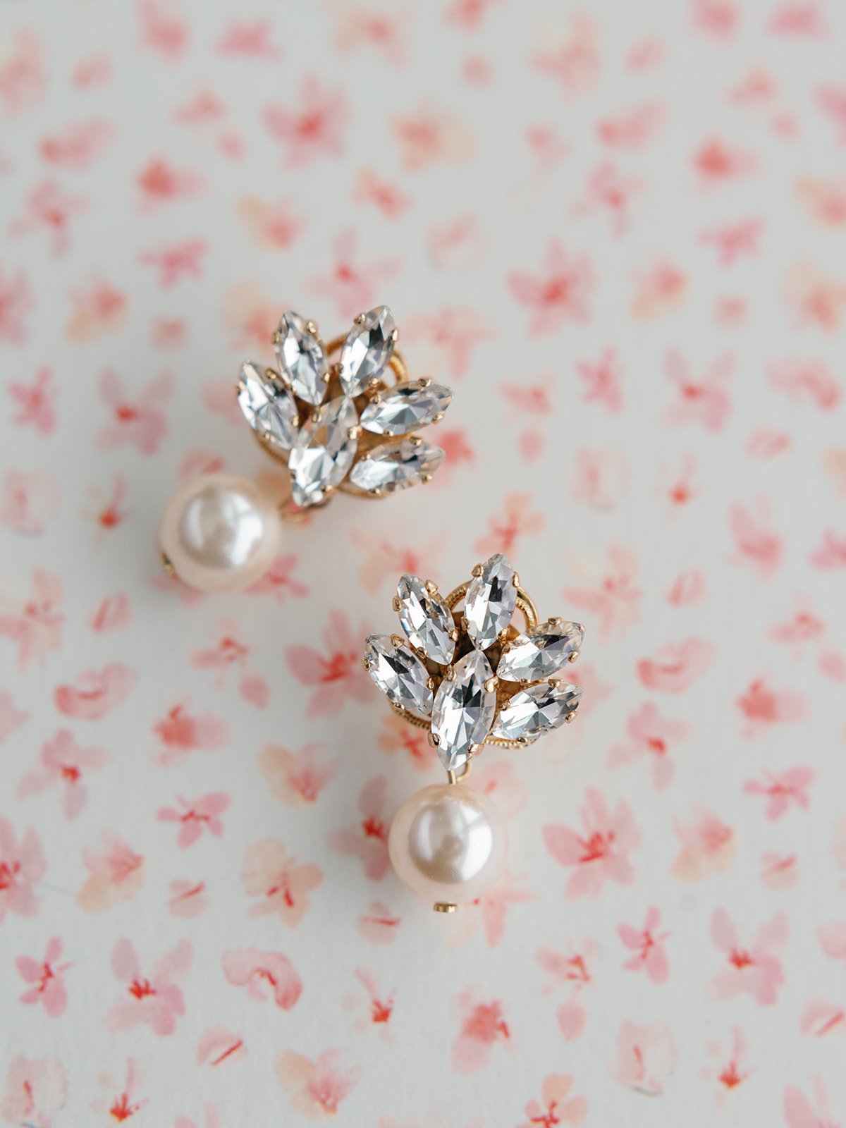 Pair of pearl and crystal leaf earrings on pink floral background.