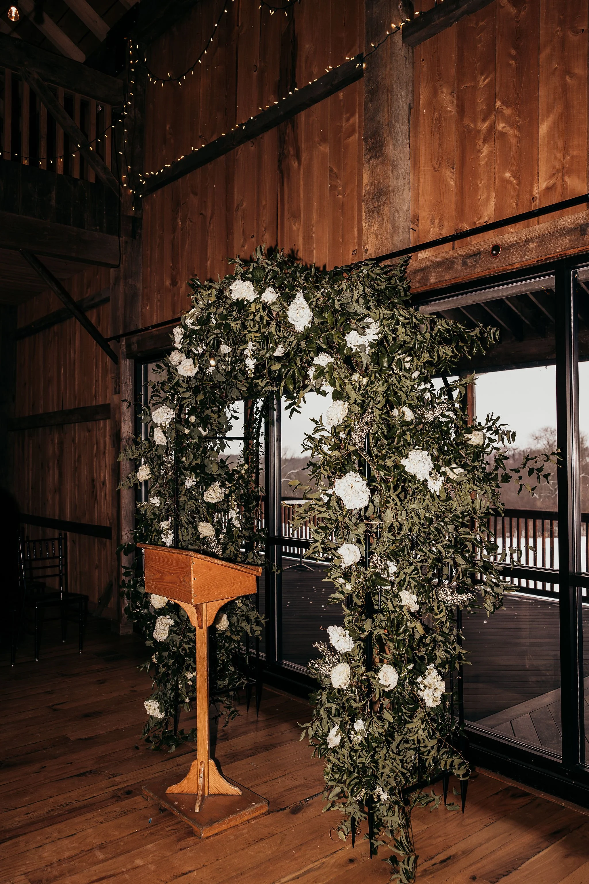 Indoor wooden space with decorative floral arrangement, a wooden lectern, and string lights on the ceiling
