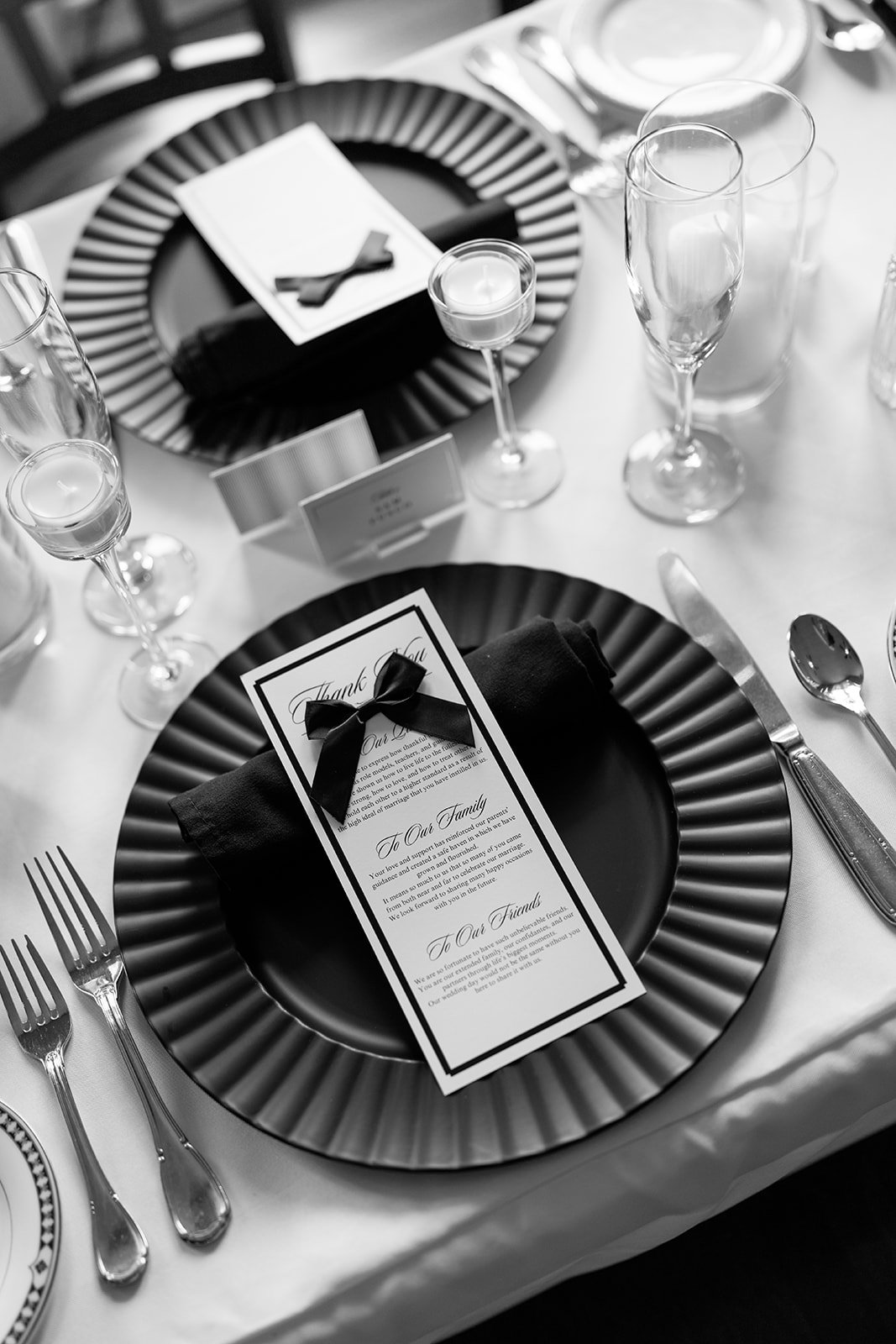 Elegant table setting with black and white striped charger plates, black napkins with ribbon, wine glasses, forks, knives, spoons, candles, and a printed menu and thank you note.