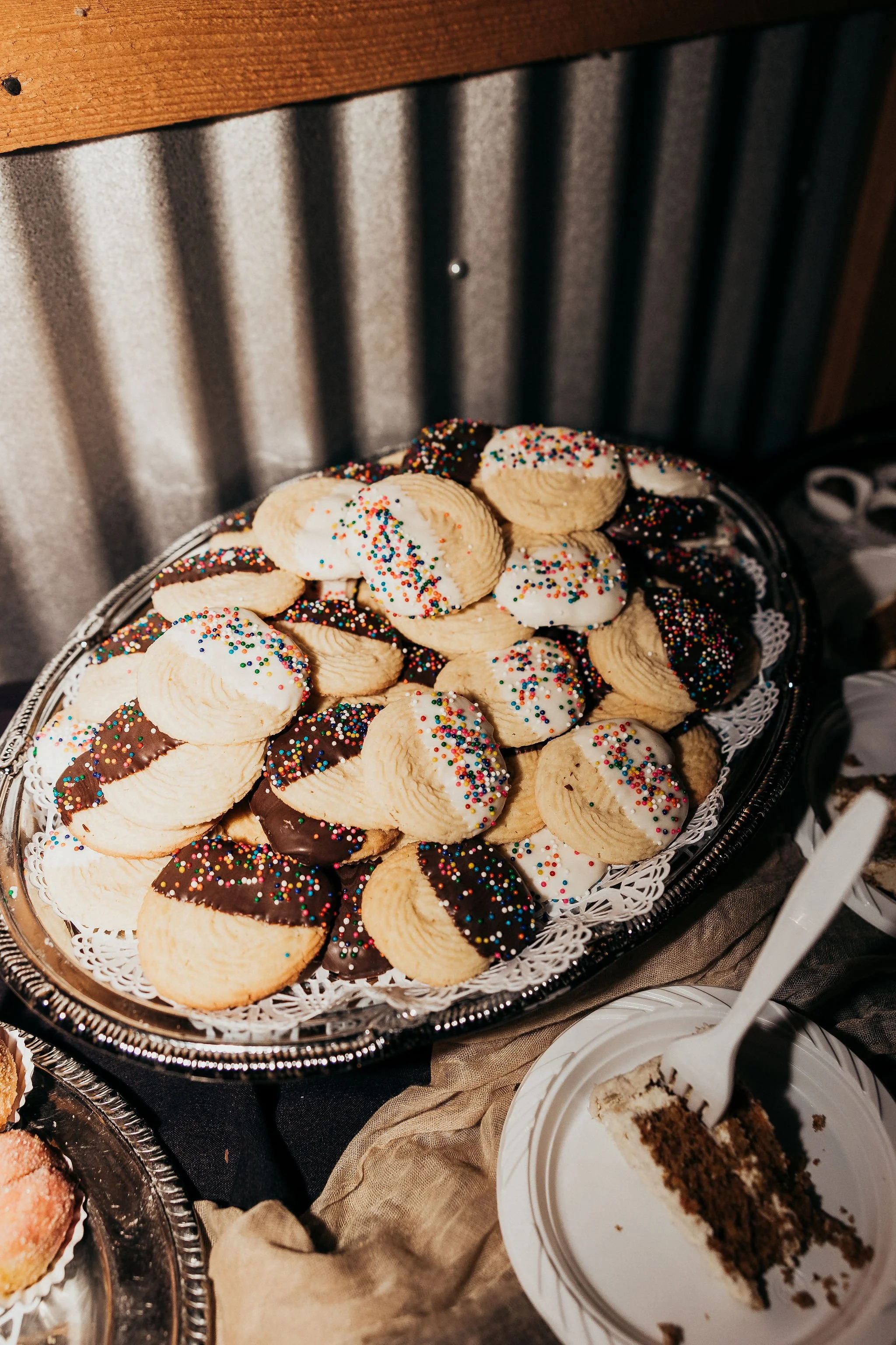 Assorted cookies with sprinkles on a silver tray and a slice of cake on a white plate.
