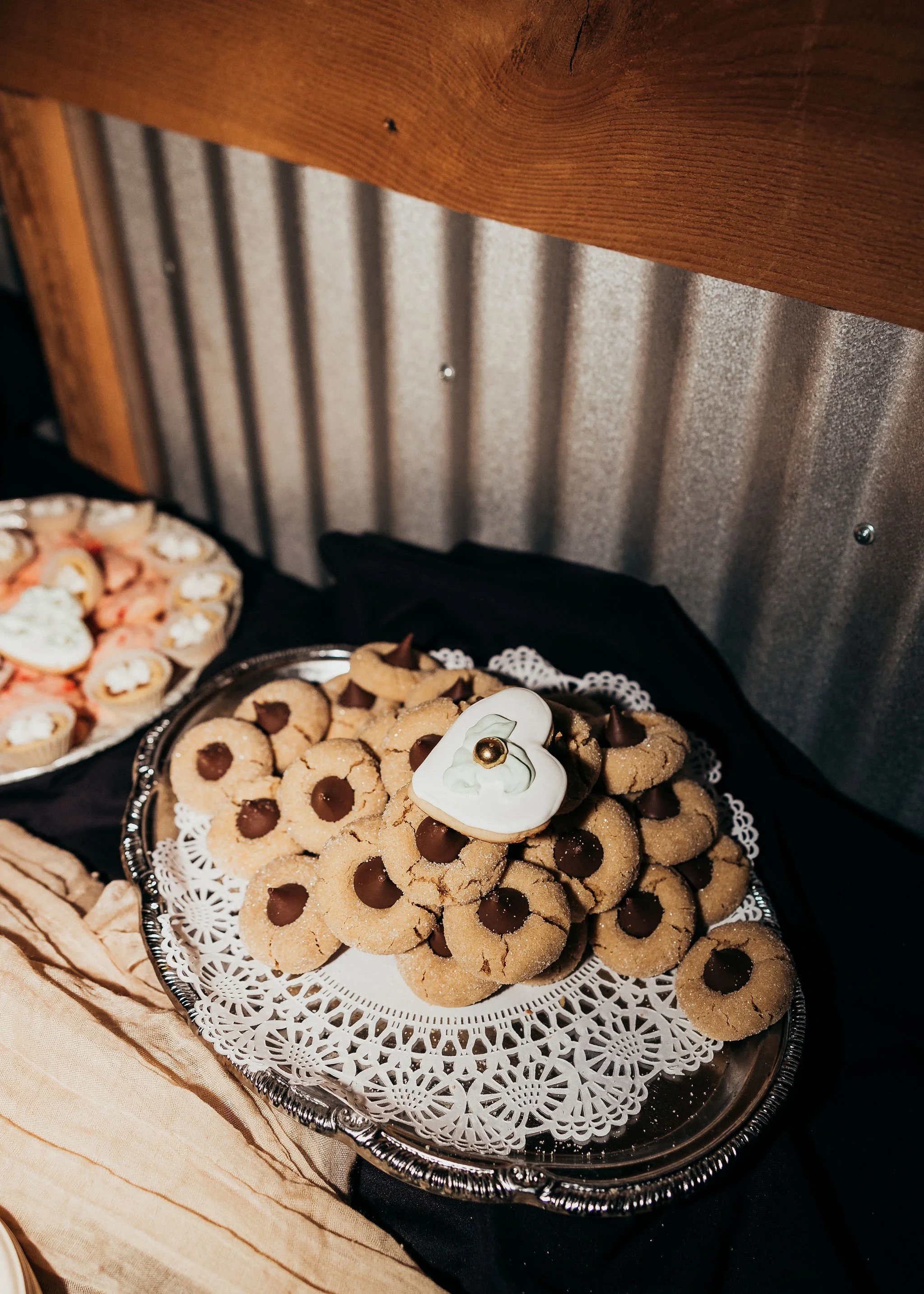 Tray of cookies decorated with chocolate chips and a white icing flower with a gold bead, placed on a doily-lined silver tray at a dessert table.