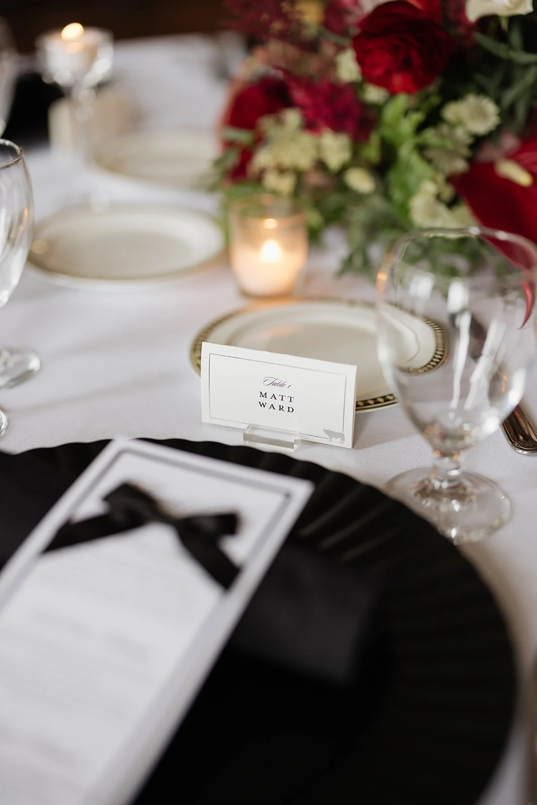 Elegant table setting with a floral centerpiece, candles, and place cards for a formal event or wedding reception.