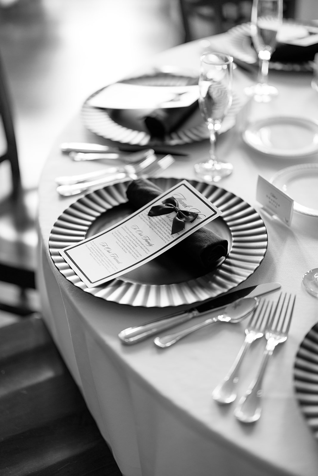 Elegant dining table setting with black and white theme. The table has plates, napkins with ribbons, utensils, wine glasses, and a place card.
