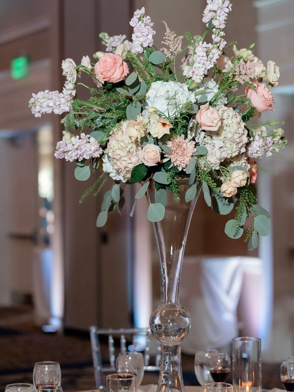 A large floral arrangement with pink and white flowers in a clear glass vase on a dining table.
