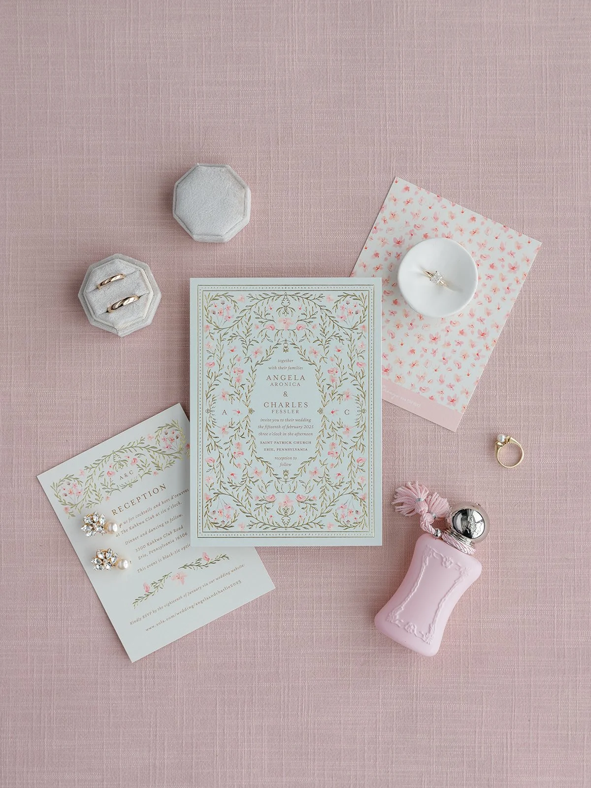 Wedding invitation floral card, pink and white floral reception card, two gold rings, pearl earrings with rhinestones, pink perfume bottle, pink keychain, pink napkin, jewelry box, ring in small white dish, octagonal jewelry box, and a pink textured 
