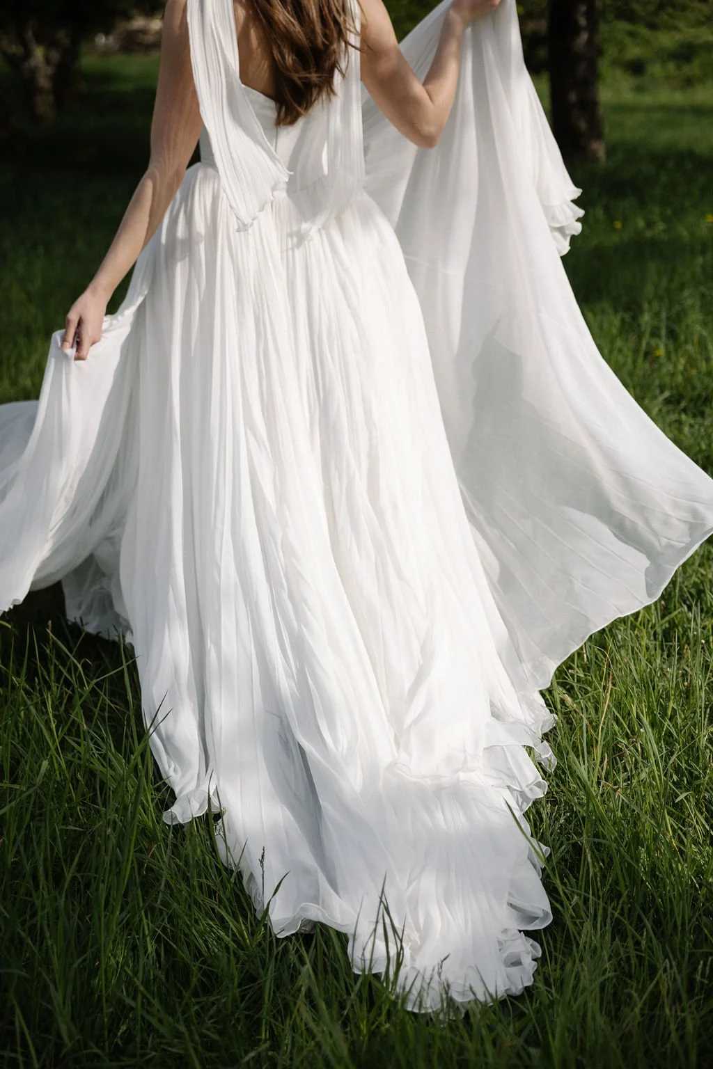 A woman in a flowing white wedding dress standing in a grassy field.