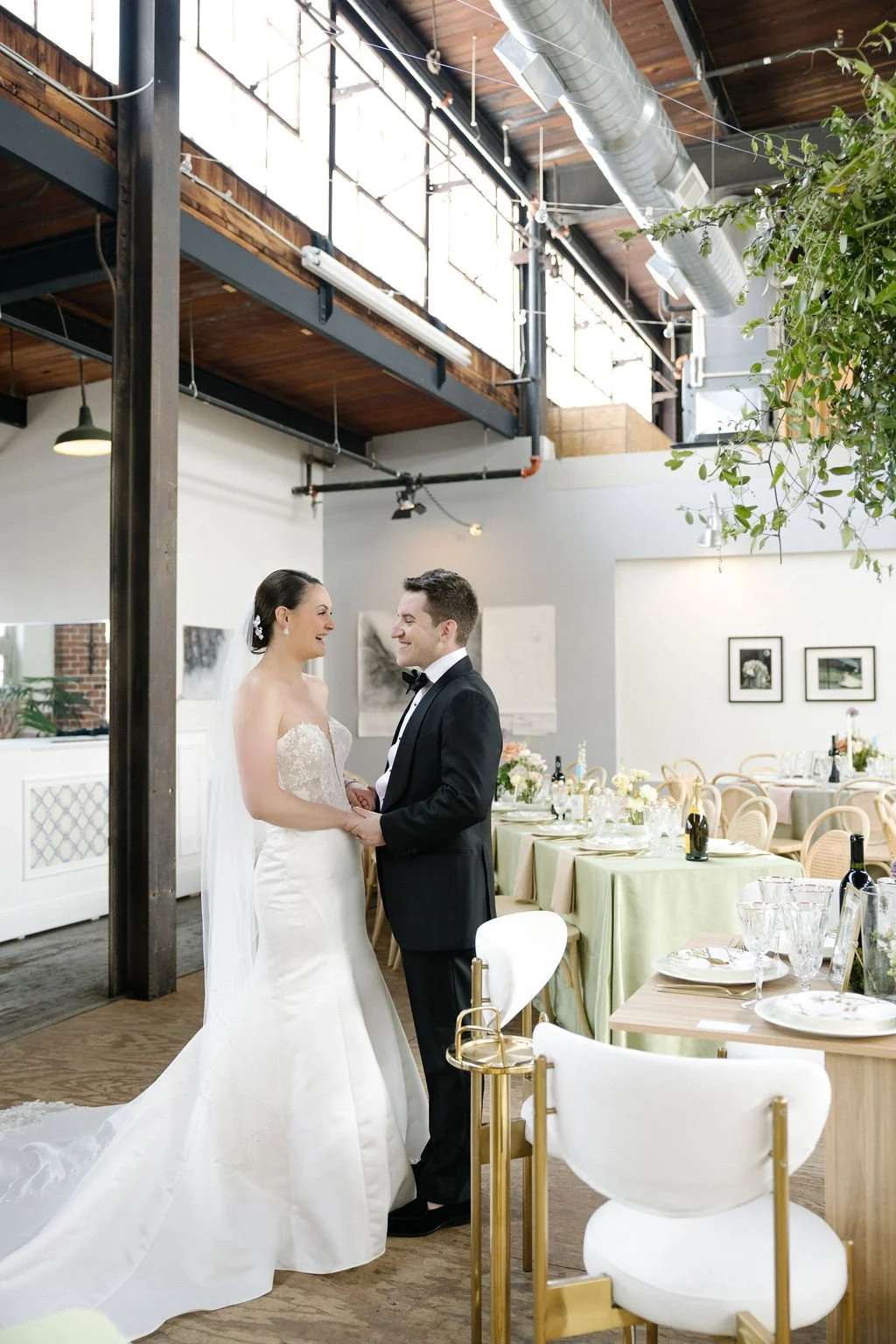 A bride and groom sharing a moment during their wedding celebration indoors, with decorated tables and artwork on the walls in the background.