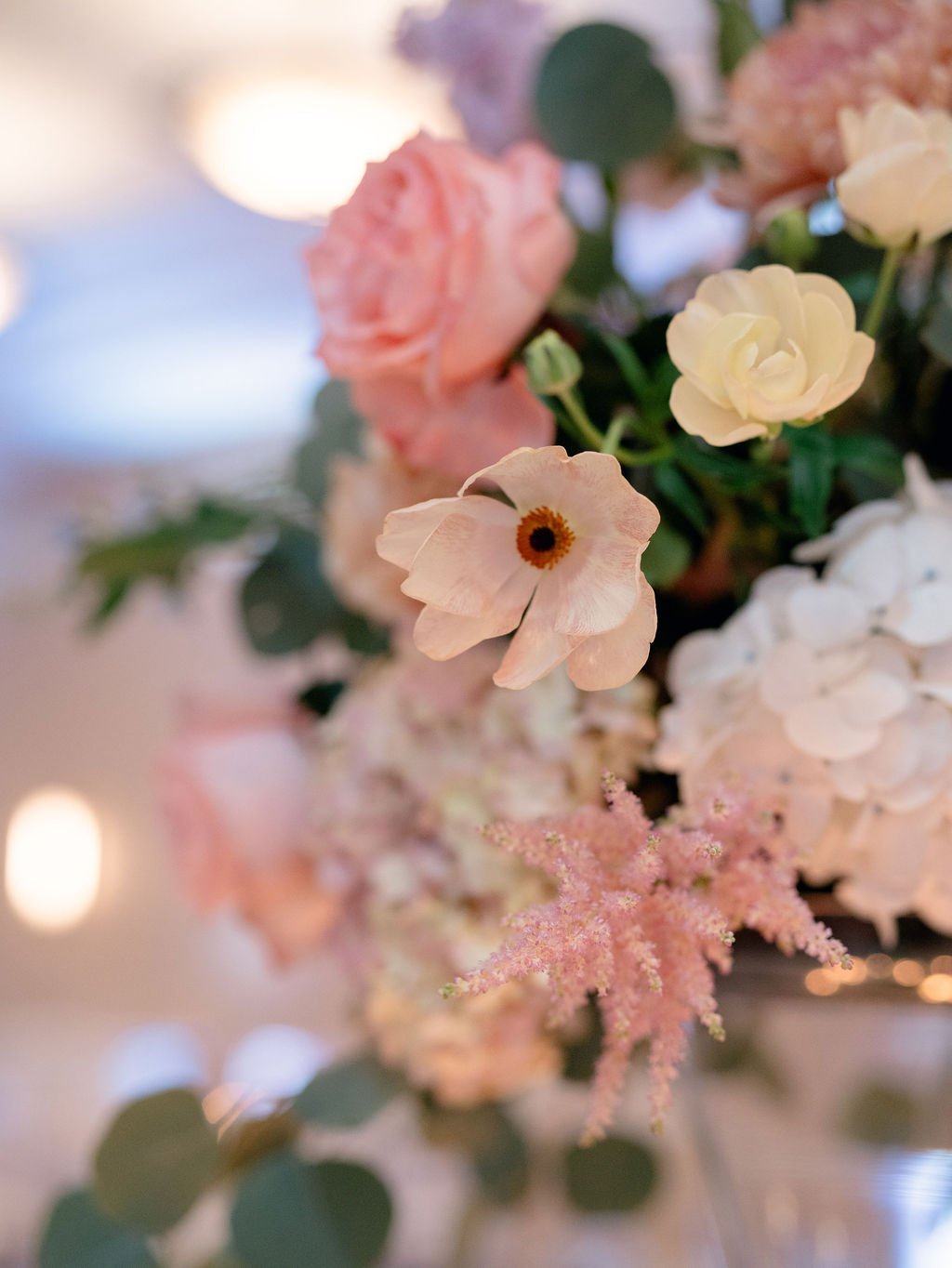 Close-up of a floral arrangement featuring pink, white, and cream-colored flowers with green leaves, slightly blurred background.