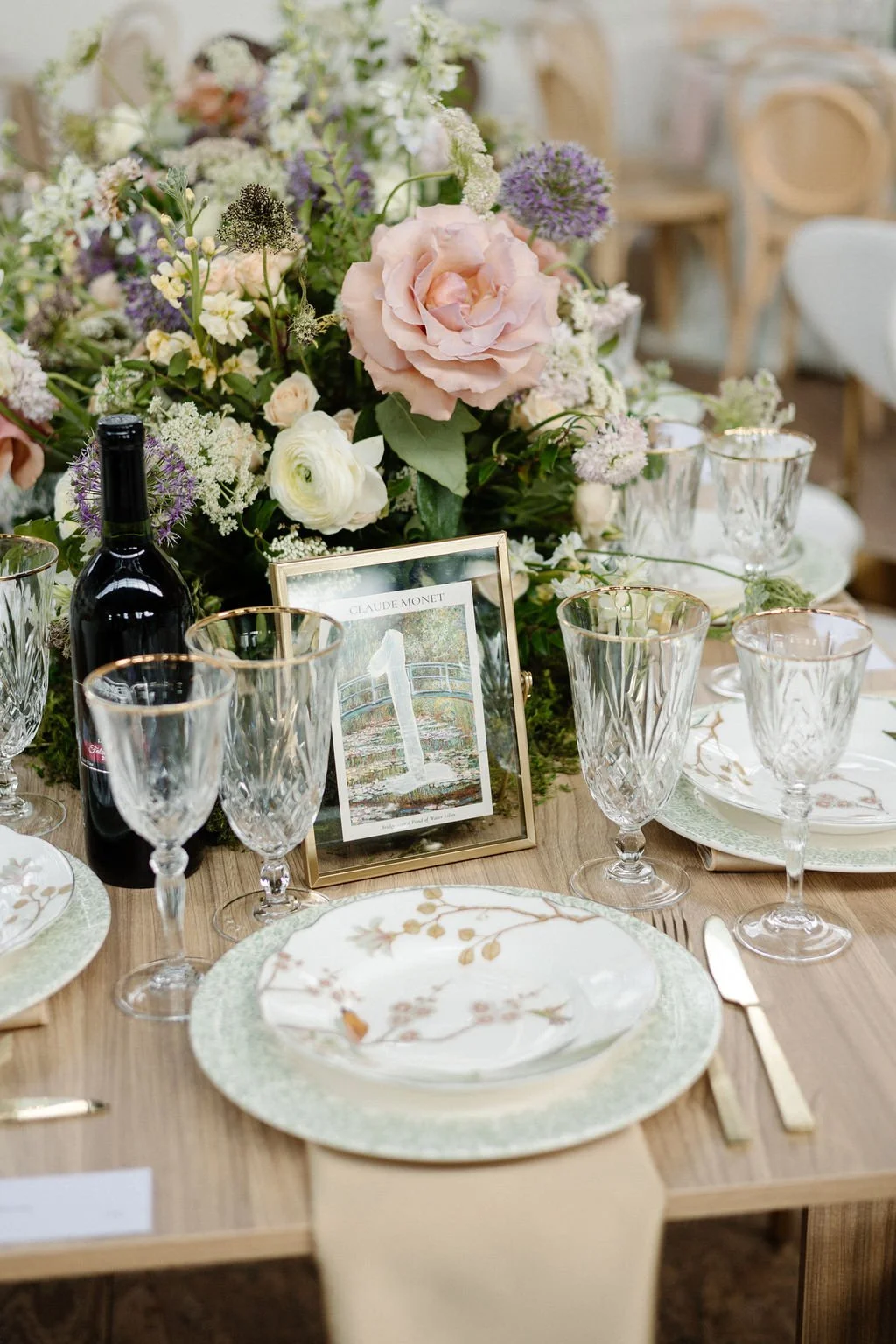 Elegant table setting with floral centerpiece, wine bottle, glassware, plates, and a framed photo at a formal event or wedding reception.