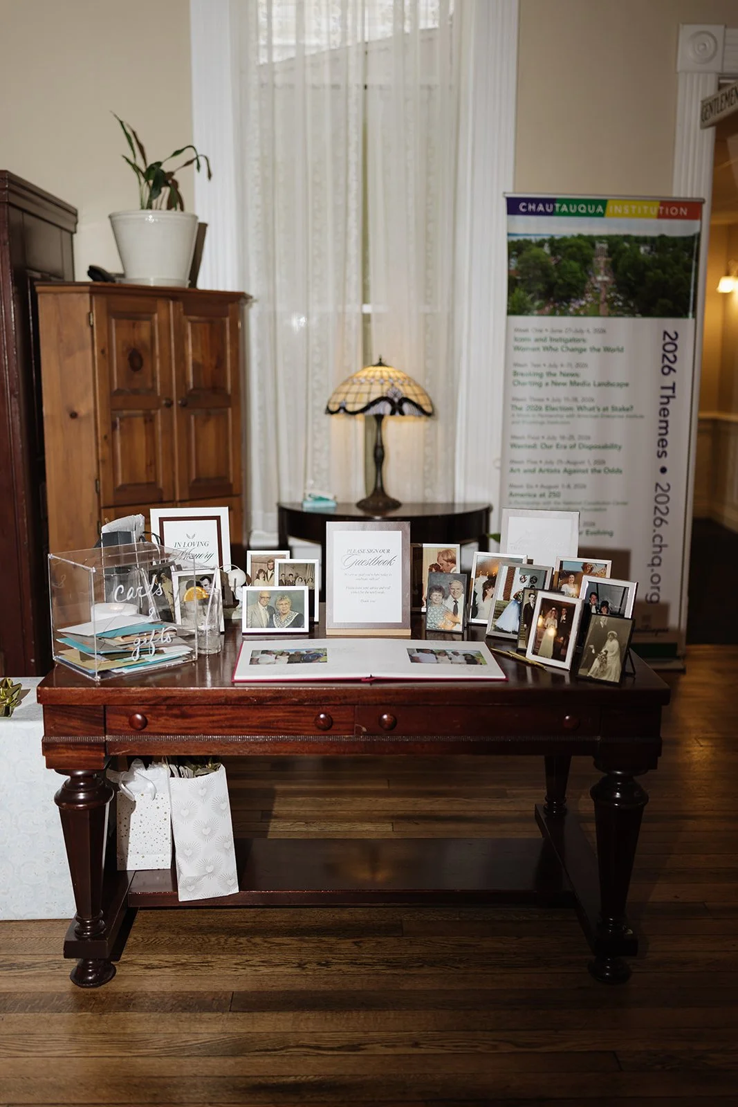 Sign-in and guestbook table at event with framed photos, cards, and a sign requesting guests to sign the guestbook.