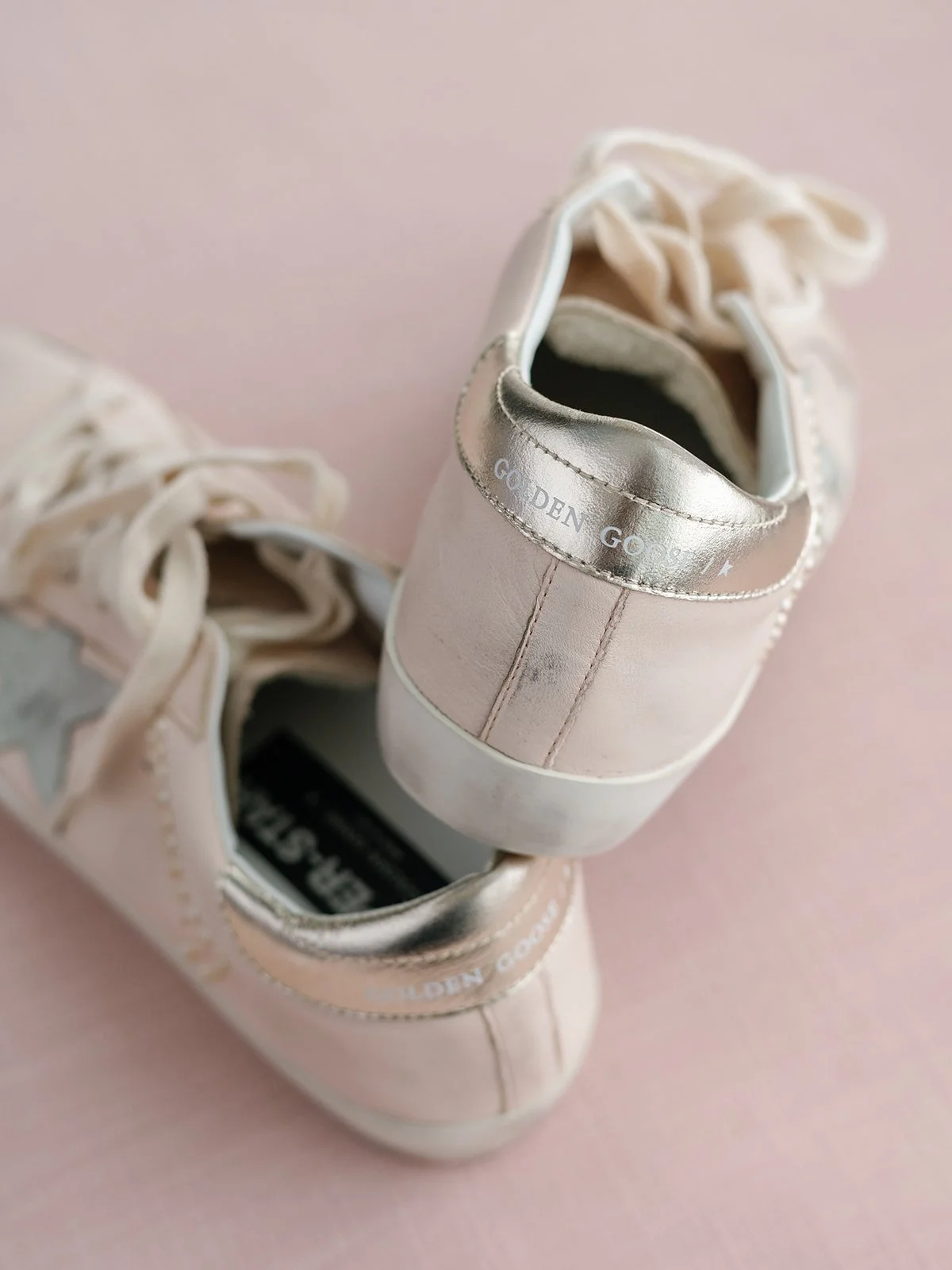 Close-up of a pair of light pink sneakers with metallic accents on a pink background.