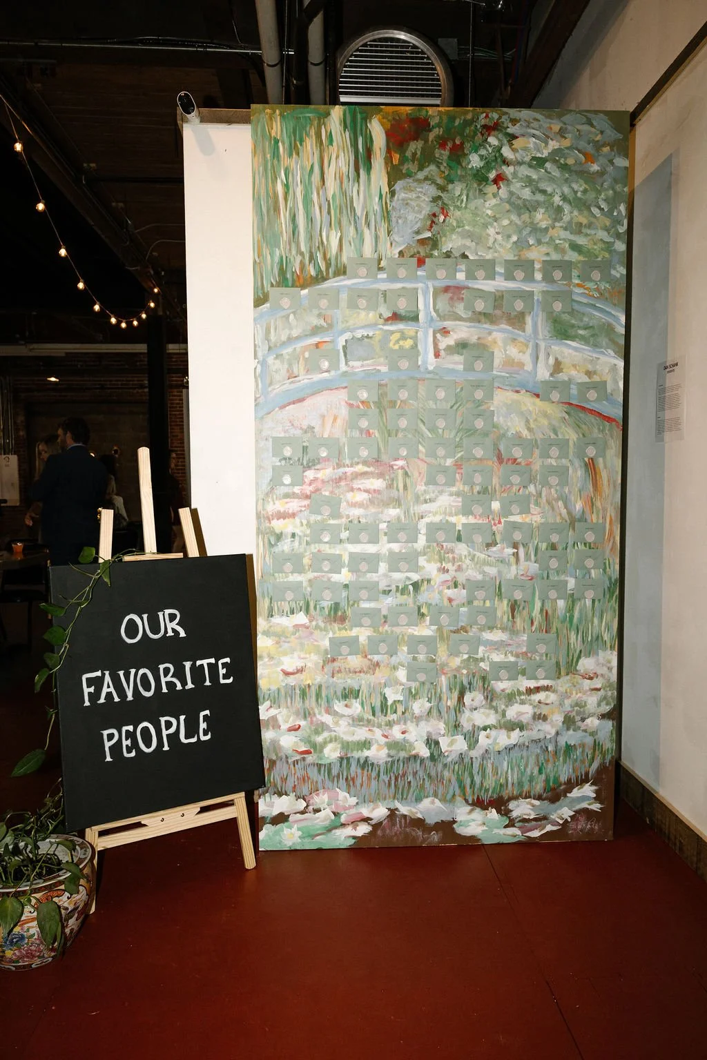A painted backdrop of a pond scene with a bridge, trees, and water lilies, equipped with small pieces of paper and a sign that reads "Our Favorite People" in a restaurant or cafe setting.