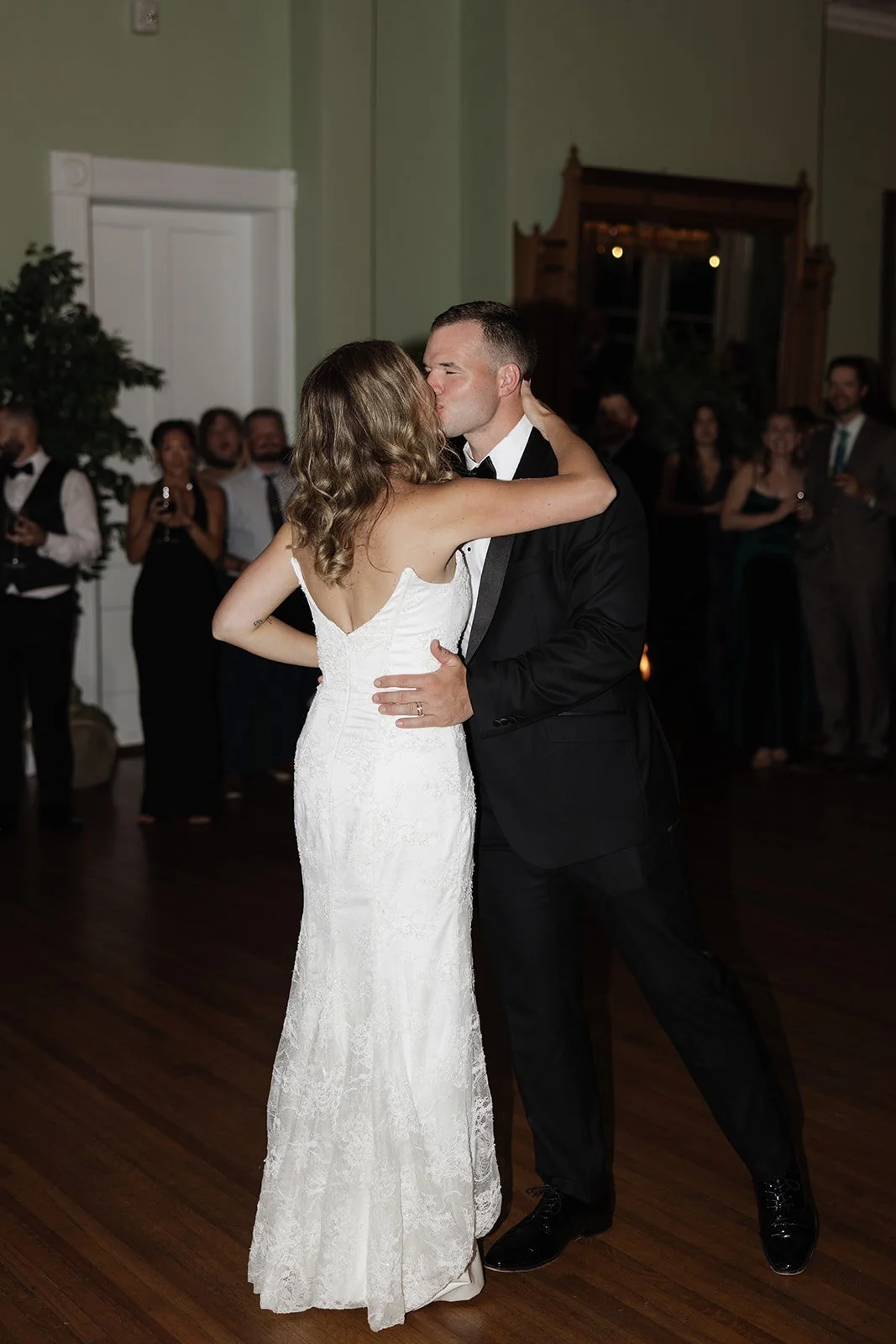 A bride and groom share a dance at their wedding reception, surrounded by guests in formal attire.