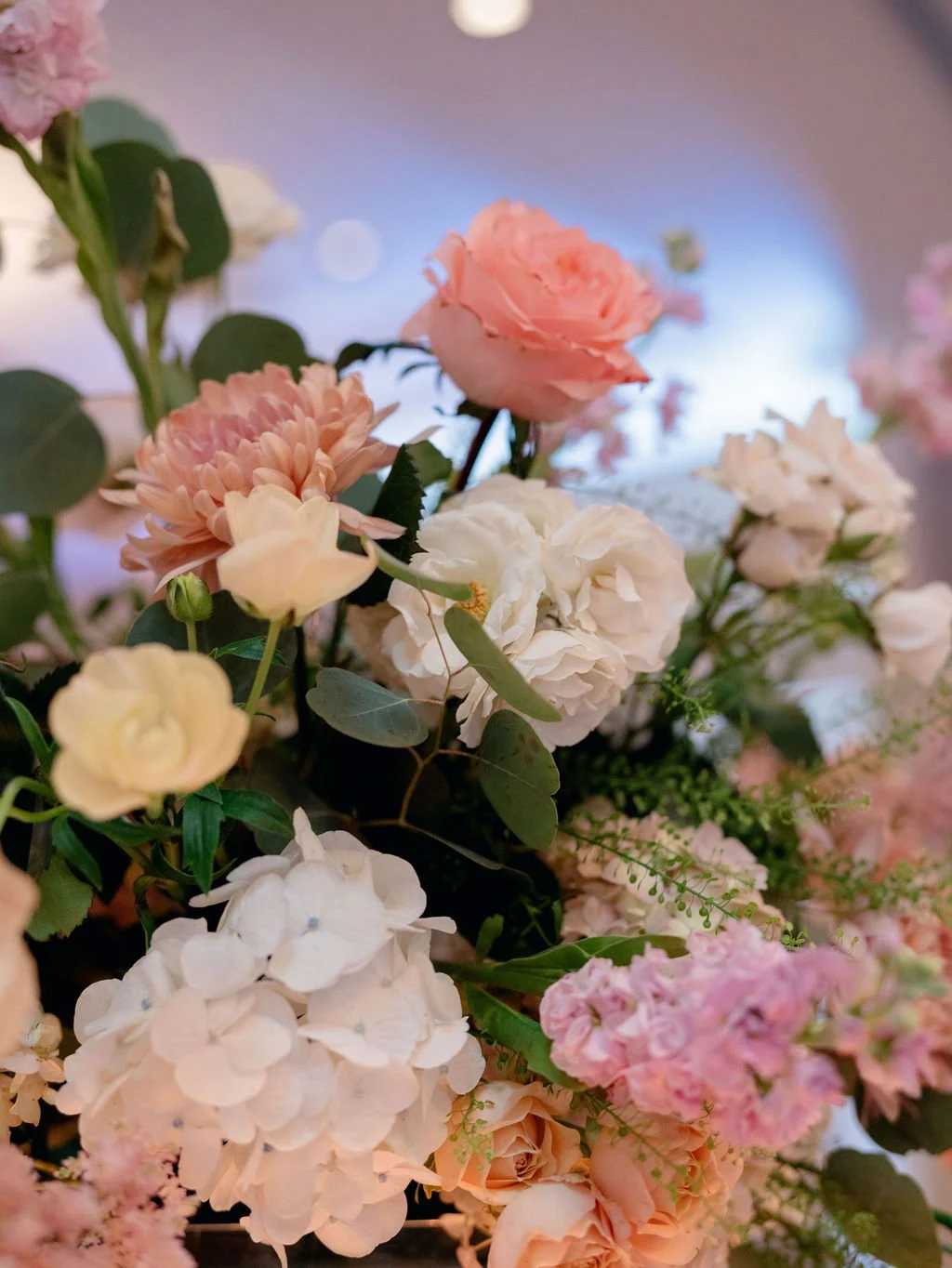 A close-up view of a colorful bouquet of various pink, white, and cream flowers with green leaves.