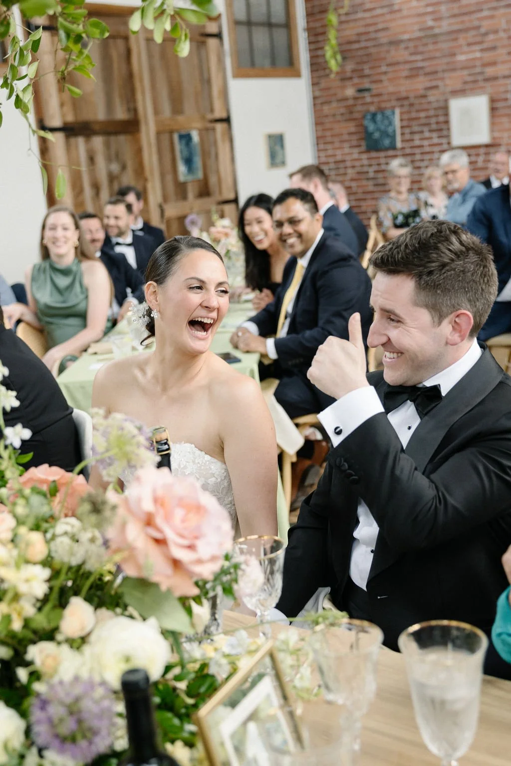 A bride and groom laughing and enjoying their wedding reception, surrounded by friends and family.