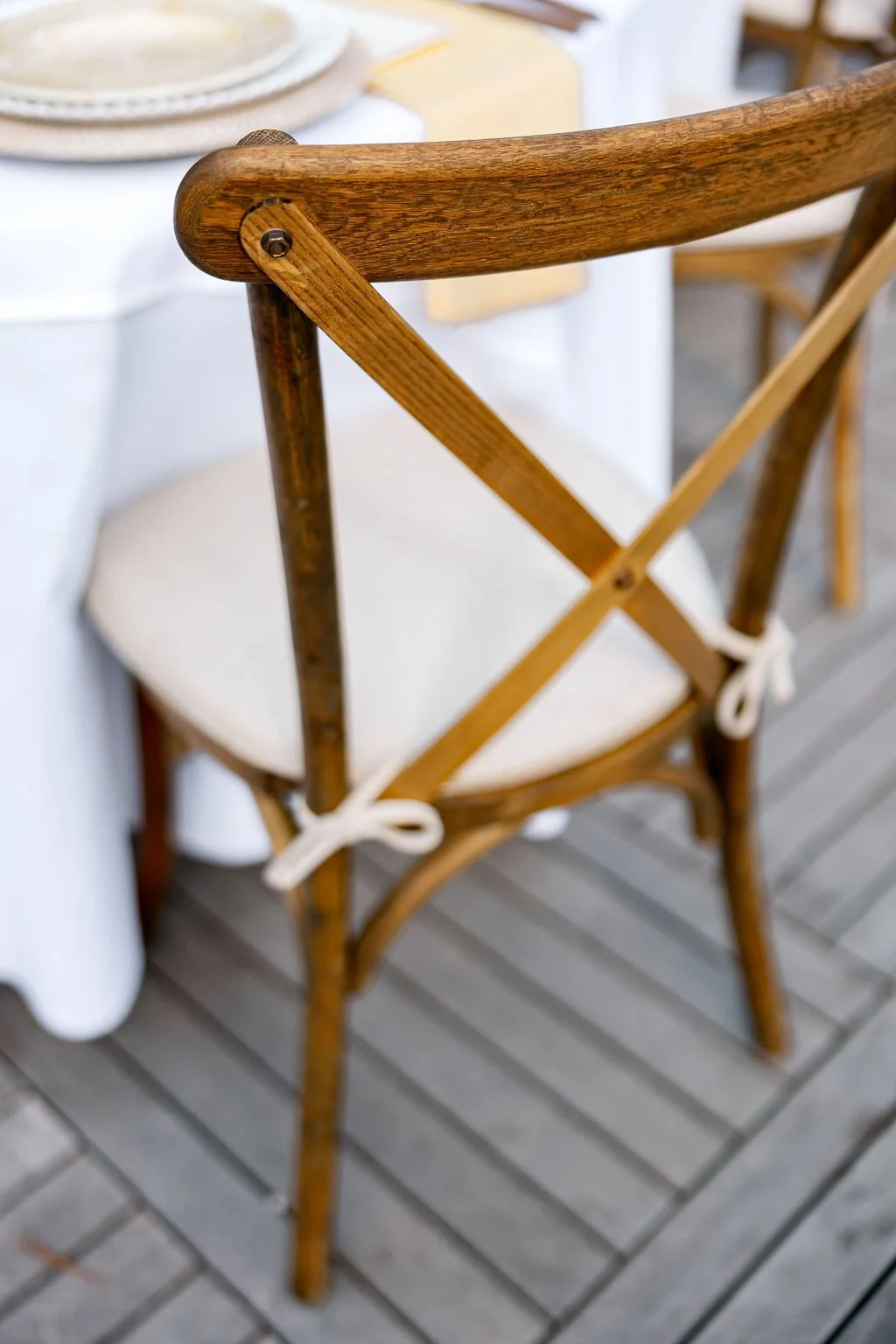 Wooden chair with a white cushion tied with white ribbons, positioned next to a table with a white tablecloth.