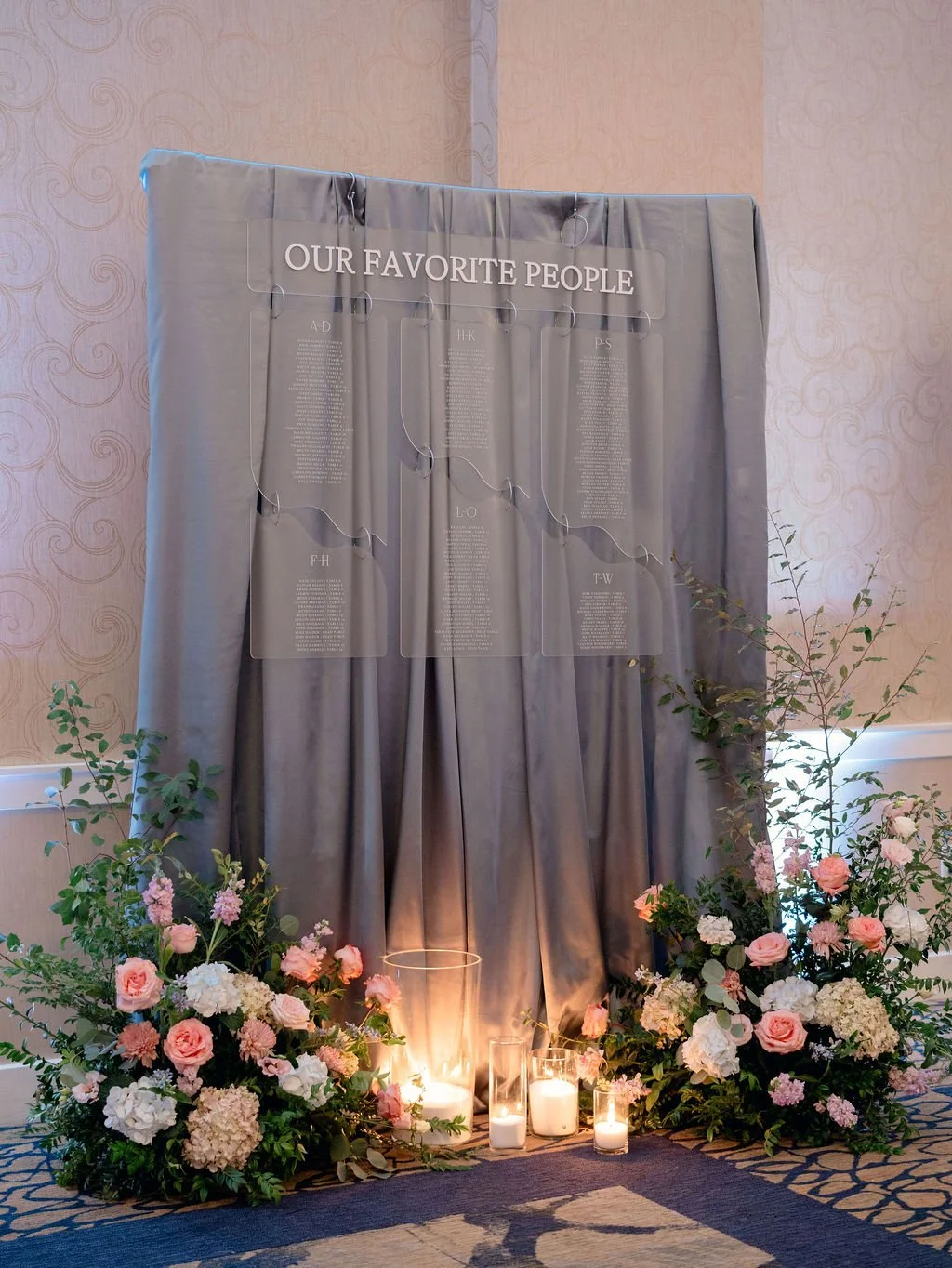 Display with flowers and candles on the floor, with a curtain backdrop and a sign that reads 'Our Favorite People', featuring a list of names or categories.