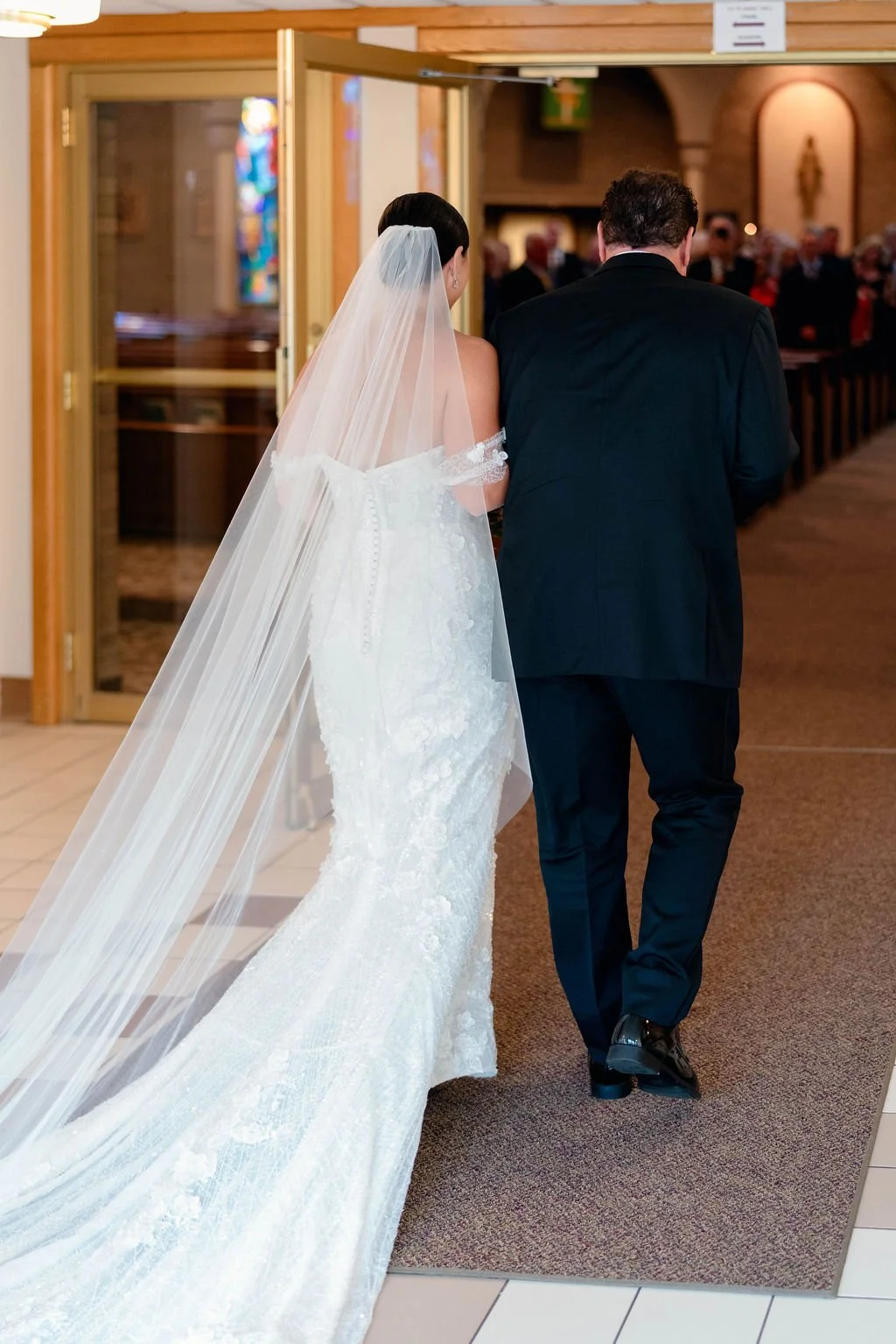 A bride and groom walking into a church wedding ceremony, with the bride wearing a white wedding gown and veil, and the groom in a black suit.