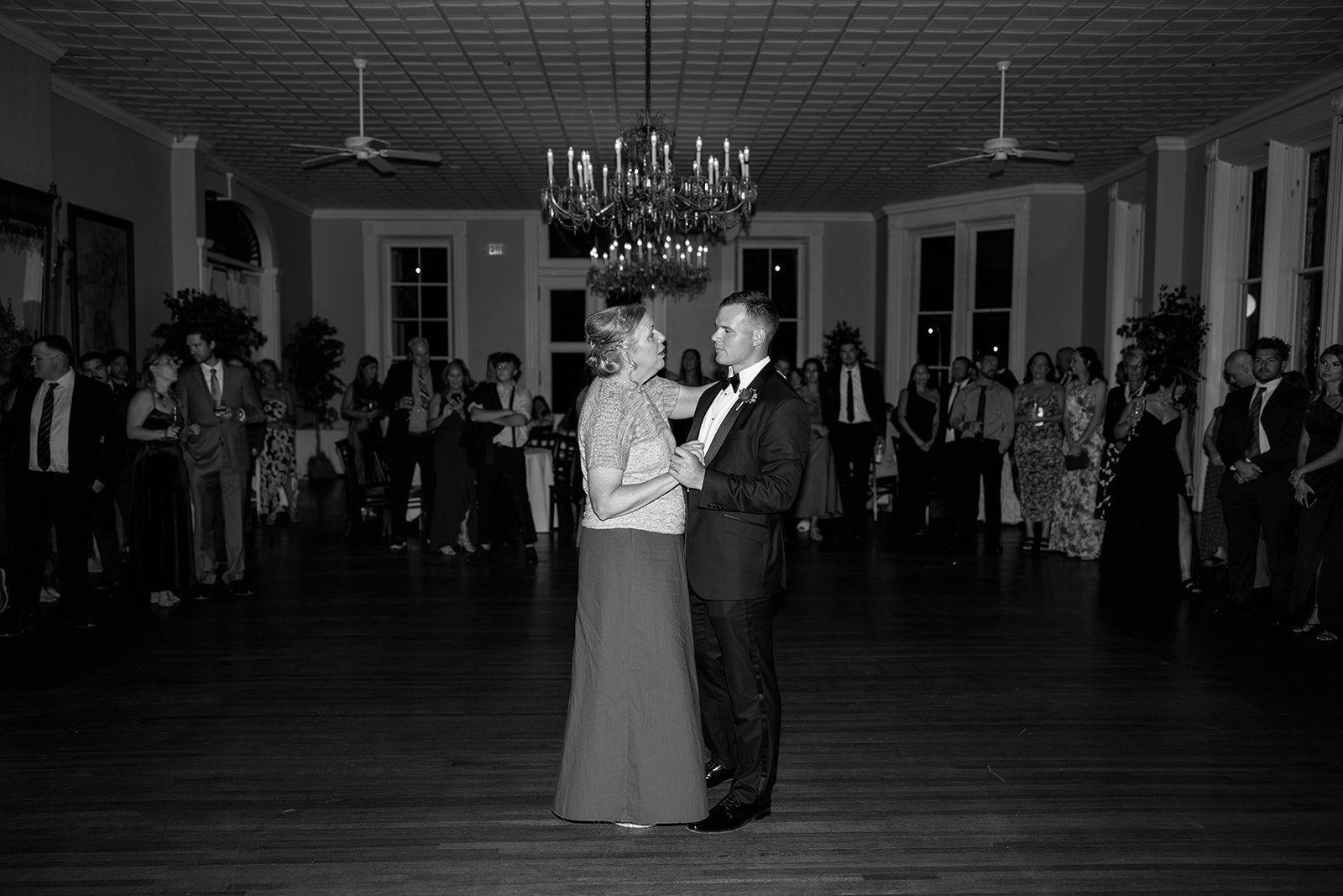 A woman and a man are dancing together in a ballroom during a wedding reception, surrounded by guests watching them.