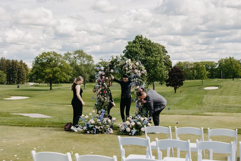 People setting up a floral arch on a golf course for a wedding ceremony.