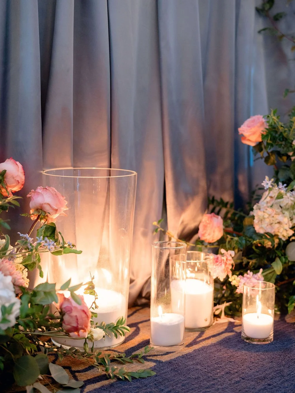 luminary candles and floral arrangements on a table against a gray curtain backdrop.