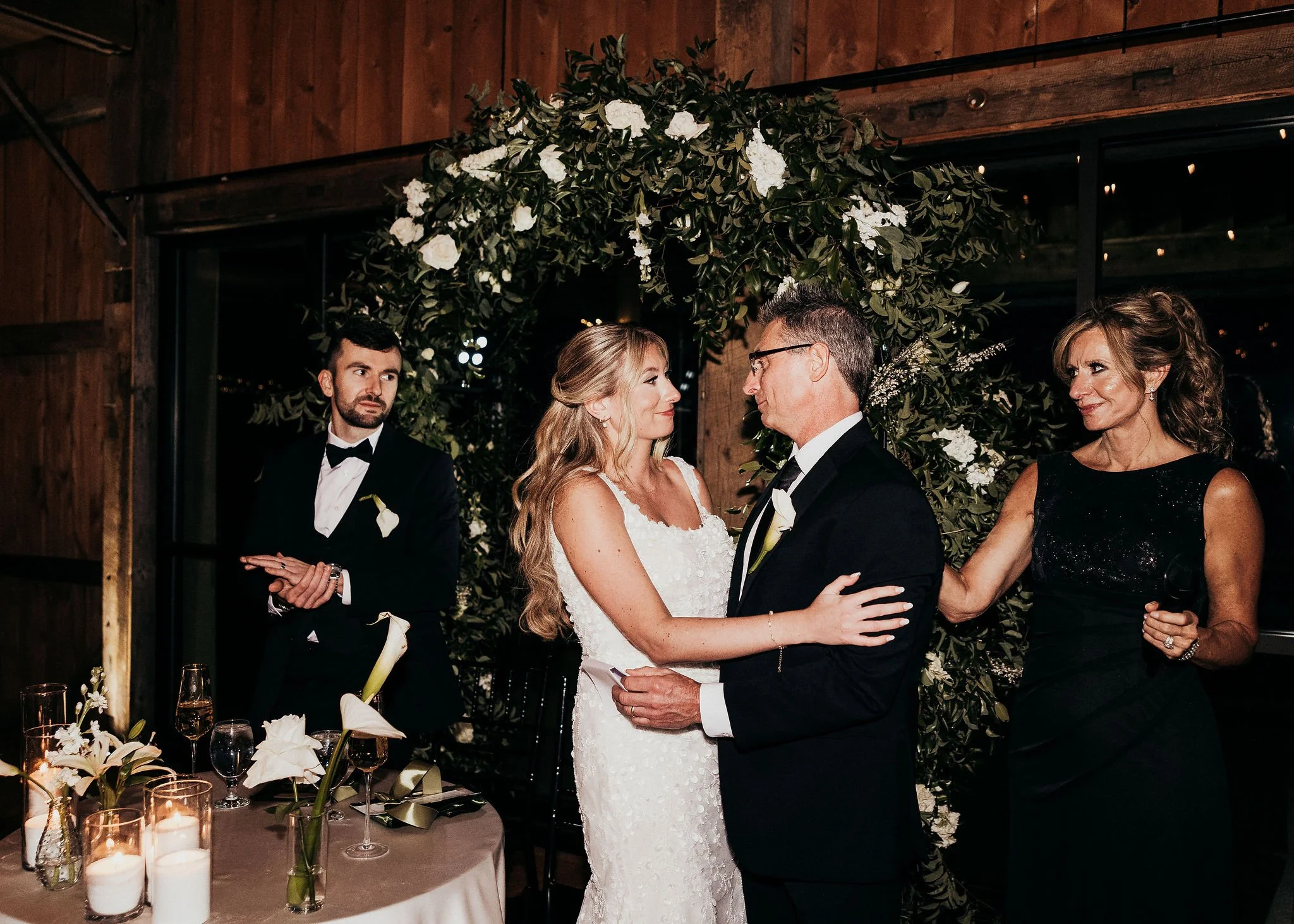 A couple getting married and exchanging vows, surrounded by family and friends in a rustic indoor setting decorated with greenery and white flowers.