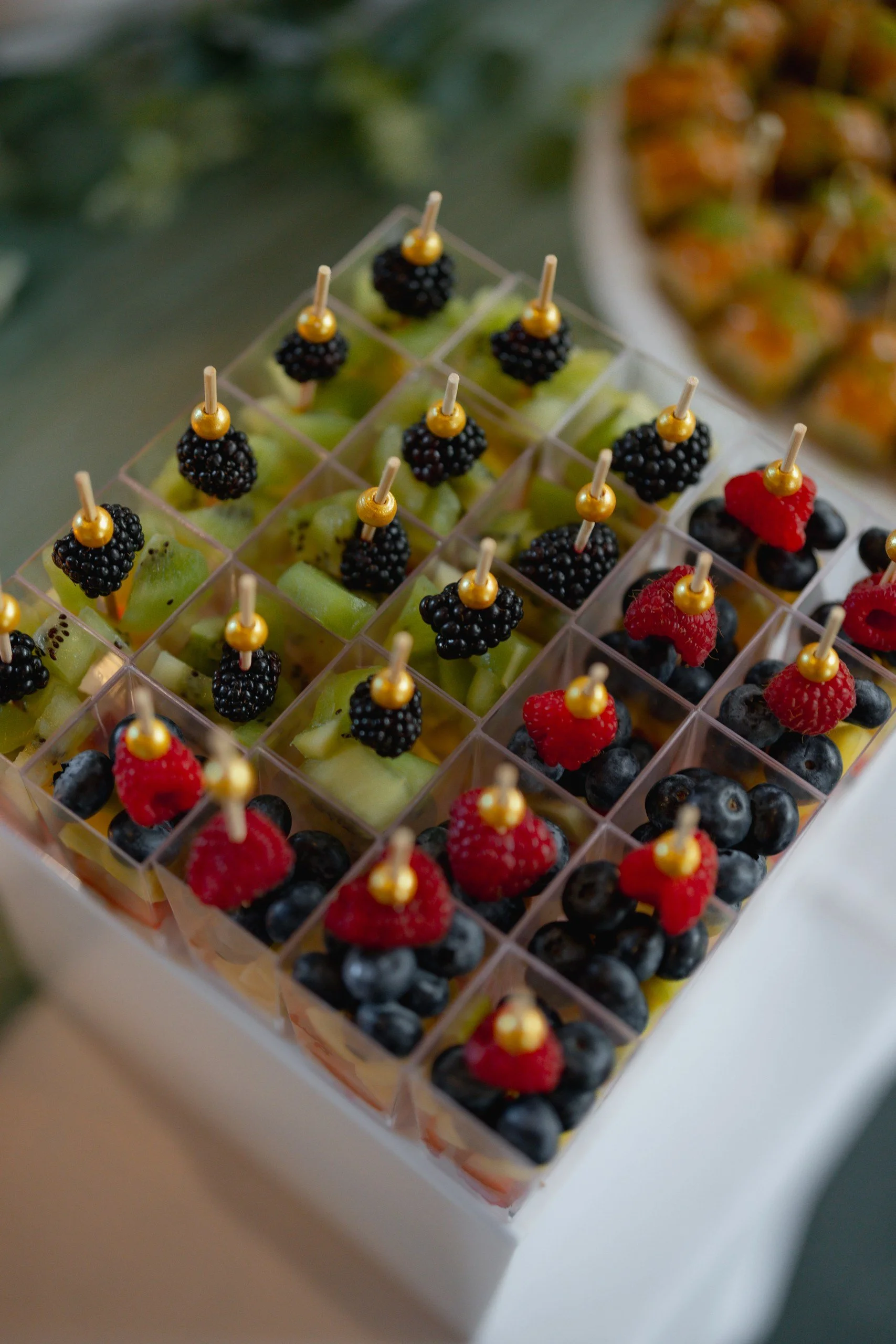 Assorted fruit skewers with blackberries, blueberries, raspberries, and grapes displayed in a plastic container.