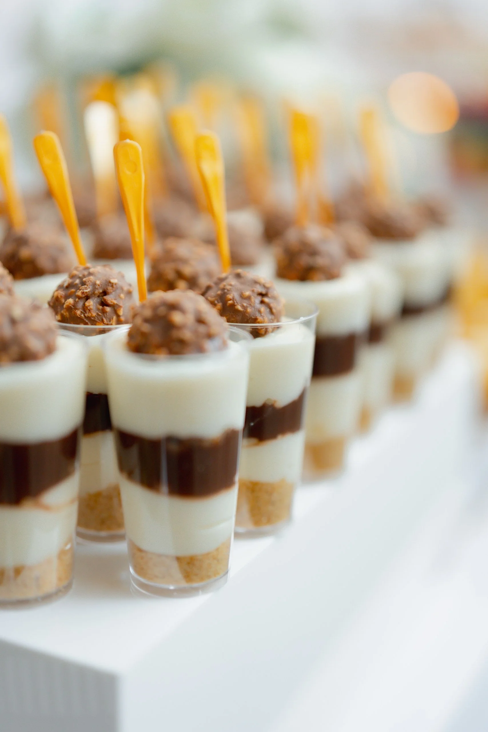 Mini dessert cups with layered ingredients, topped with a chocolate ball and a yellow spoon inserted.