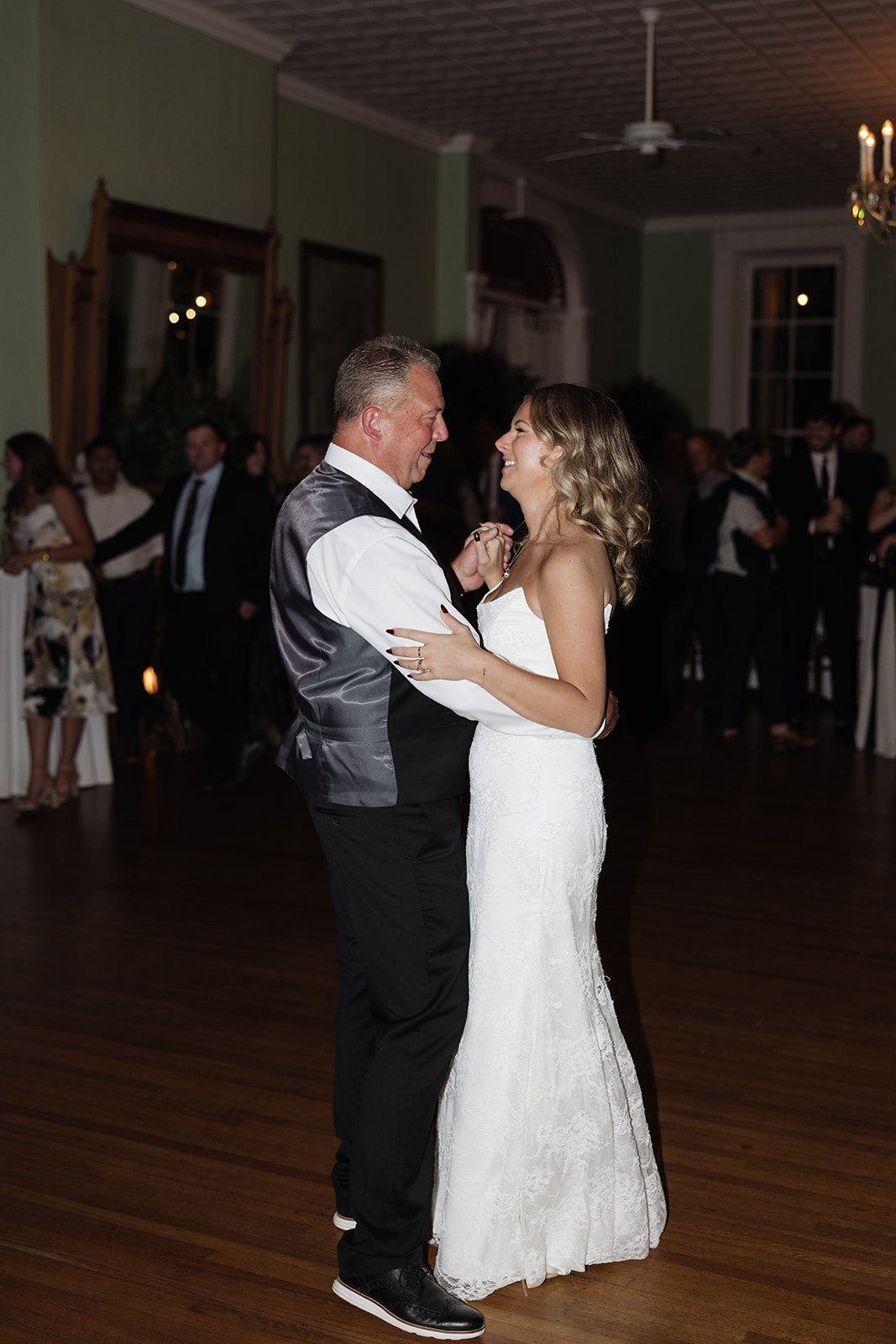 A bride and groom dancing at their wedding reception with guests in the background.