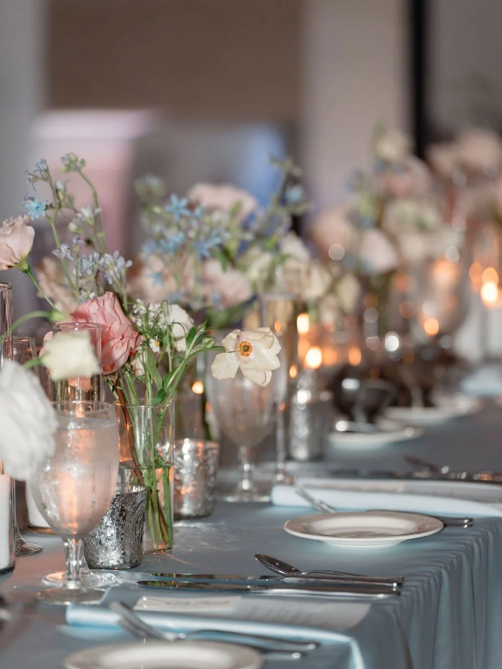 Elegant dinner table with floral centerpieces, votive candles, and place settings.