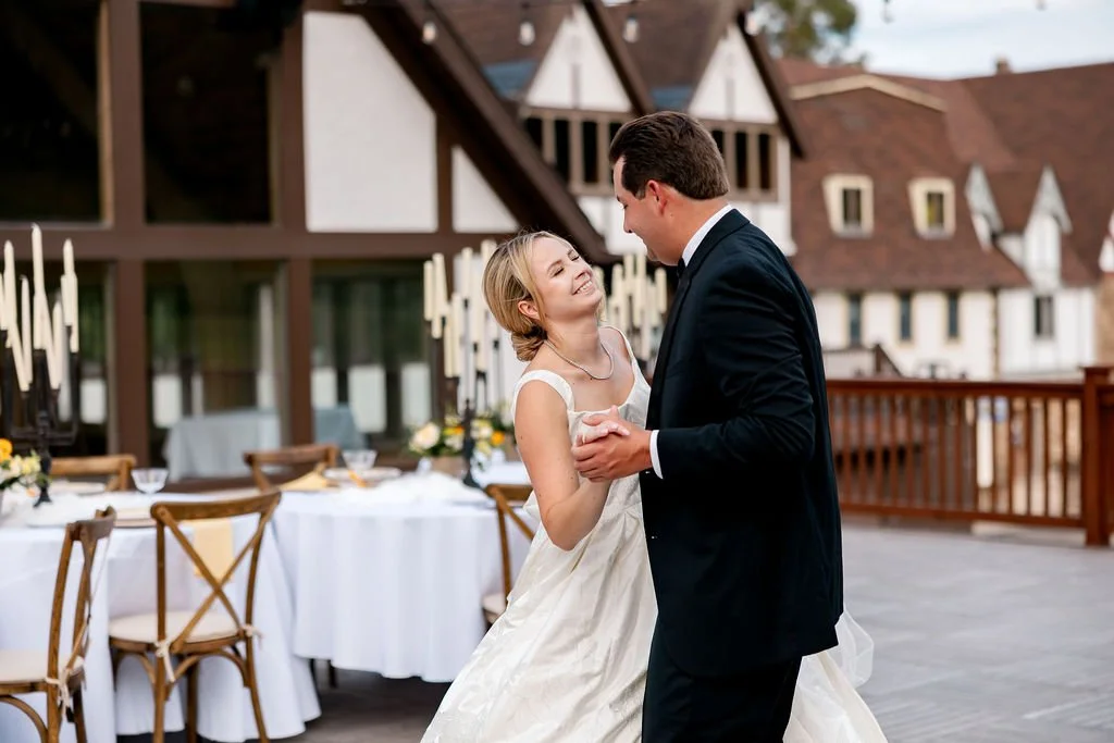 A bride and groom dancing at their wedding reception outdoors, with decorated tables and a house in the background.