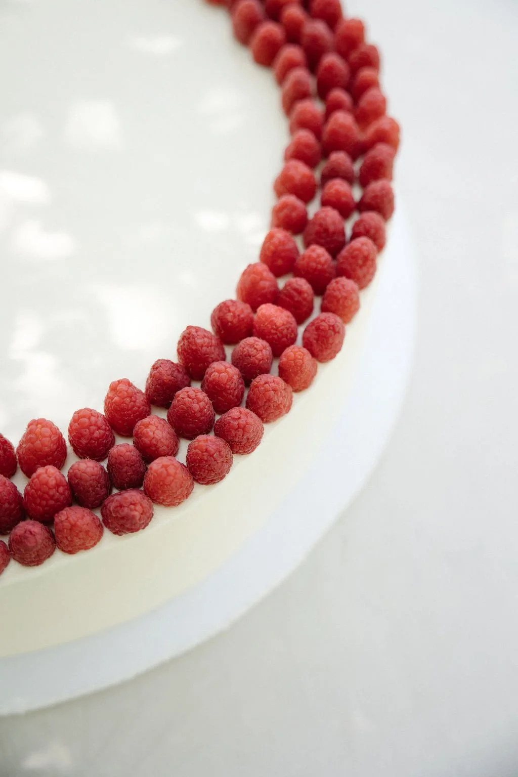 Close-up of a white cake decorated with a border of fresh red raspberries.
