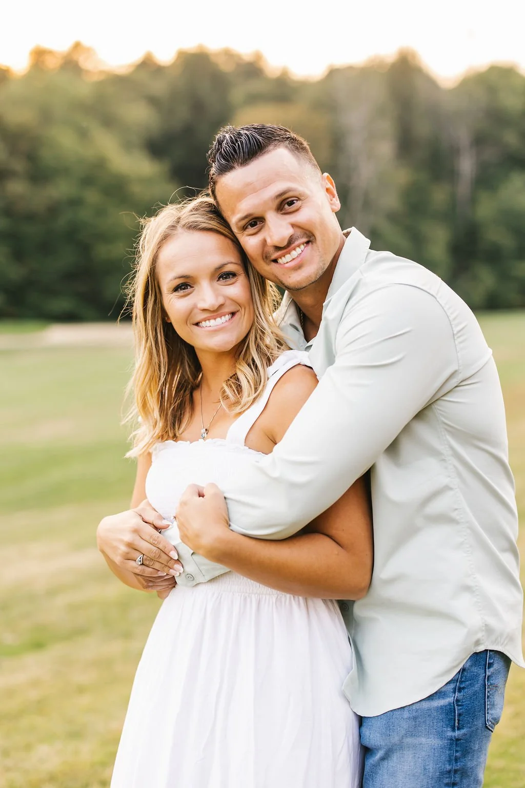 A happy couple smiling and embracing outdoors with a blurred green forest background.