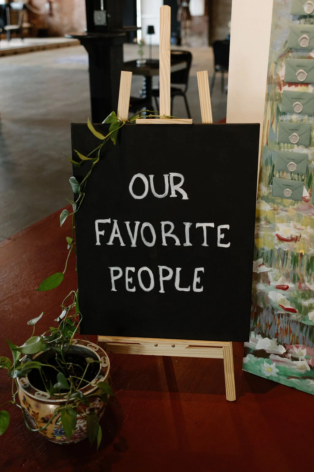 A blackboard sign on a wooden easel reads 'Our Favorite People' in white handwritten letters. A small potted plant with green leaves sits in front of the easel.