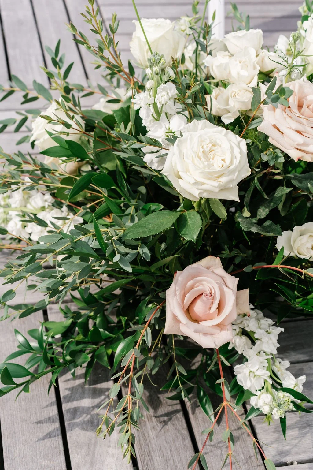 A bouquet of white and blush pink roses with green foliage on a wooden surface.