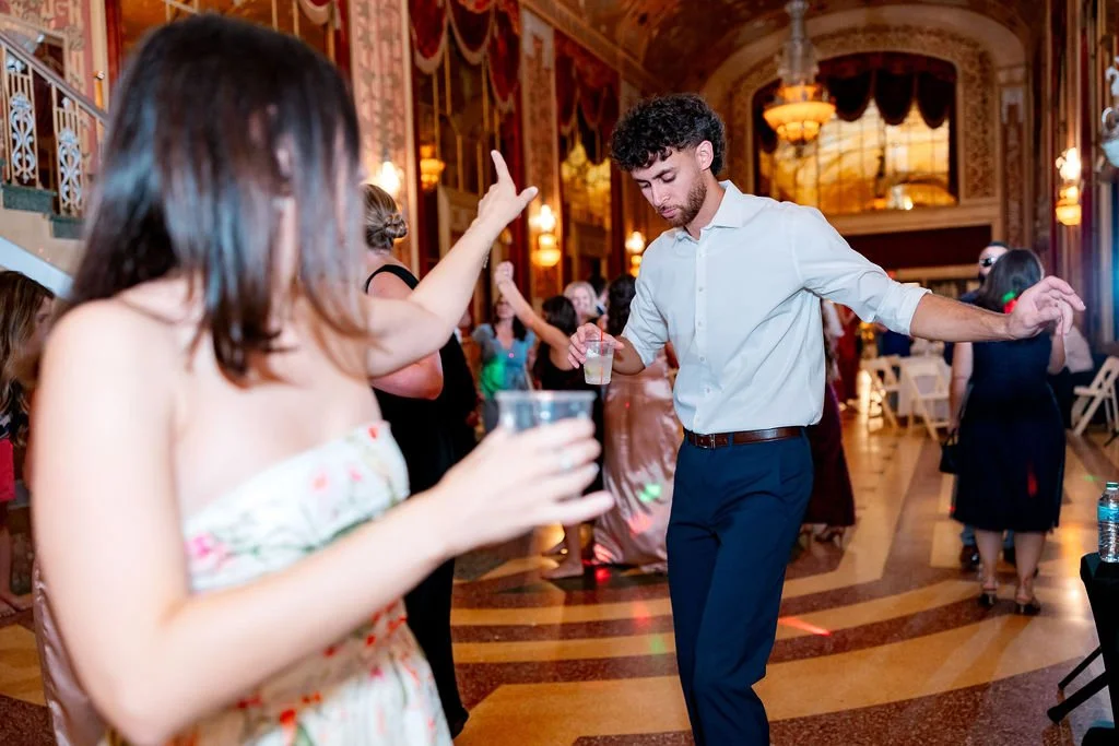 People dancing and socializing at an elegant indoor event with ornate decor, chandeliers, and warm lighting.