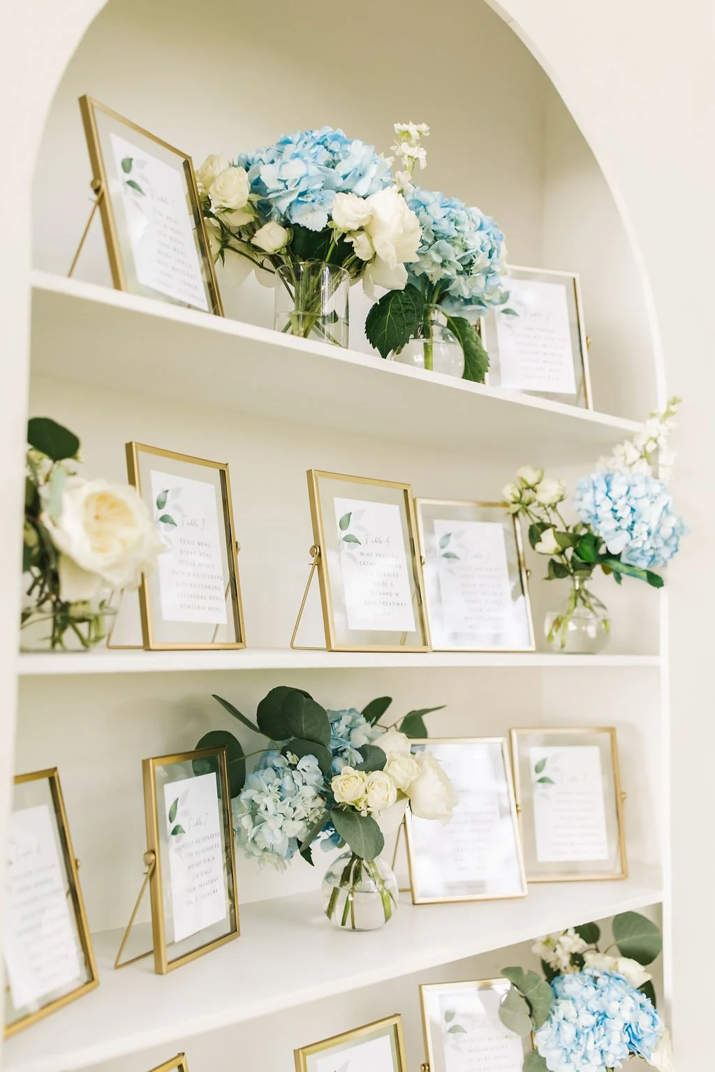 White shelves displaying framed signs and vases with blue and white hydrangeas and roses.
