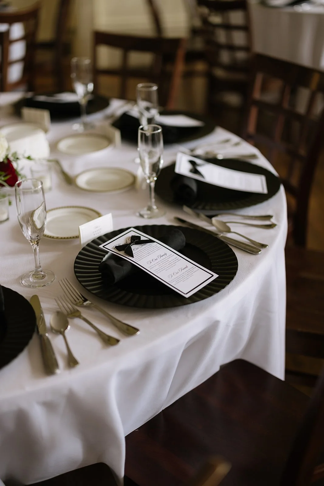 A formal dining table set for a special occasion, with black and white color themed place settings, champagne flutes, and printed menus, in a wood-paneled room.