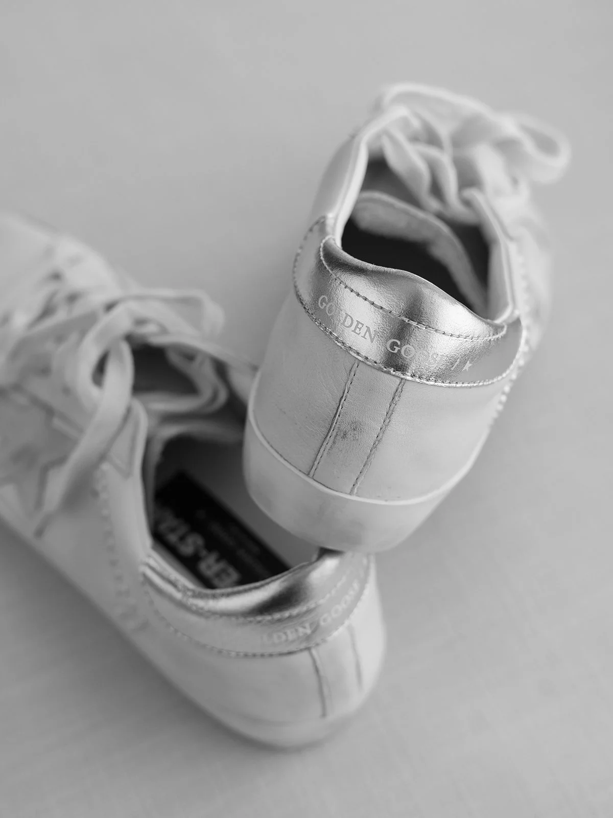 A pair of white sneakers on a plain surface, with the focus on the back of the right shoe showing text that reads 'GO DEN GO'.